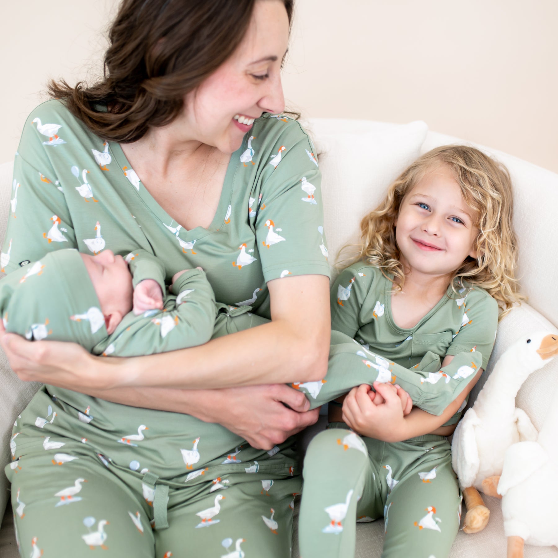 Close up of family of three matching in Silly Goose sitting on a couch. Pictured are the Take Me Home Set in Silly Goose, women's v-neck, women's lounge pants and short sleeve with pants pajama set