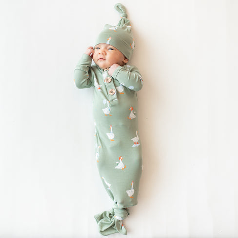 Infant shown wearing the Knotted Gown with Hat Set in Silly Goose while laying on a light colored background