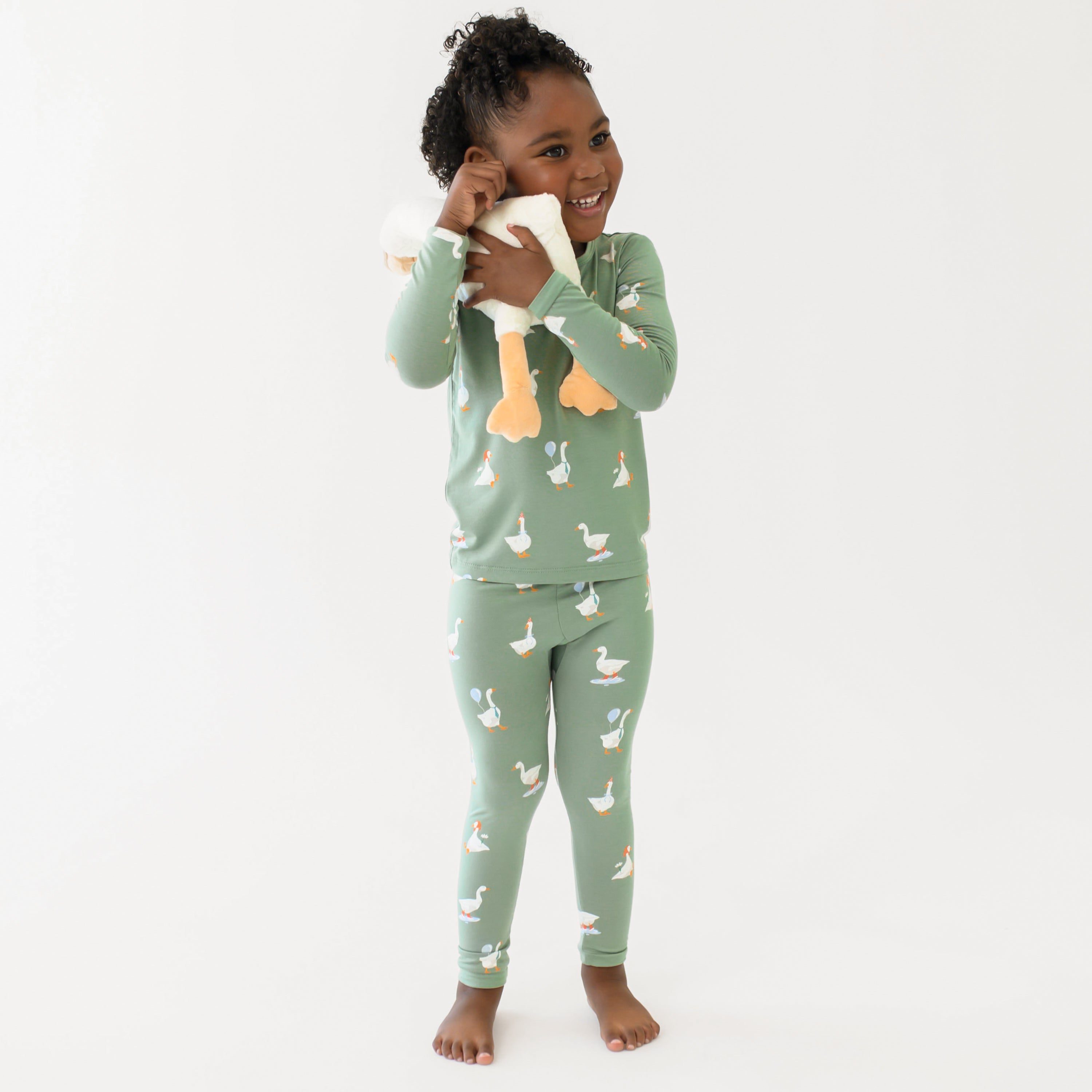 Smiling girl hugging a toy stuffed goose to her face wearing the Long Sleeve Pajamas in Silly Goose