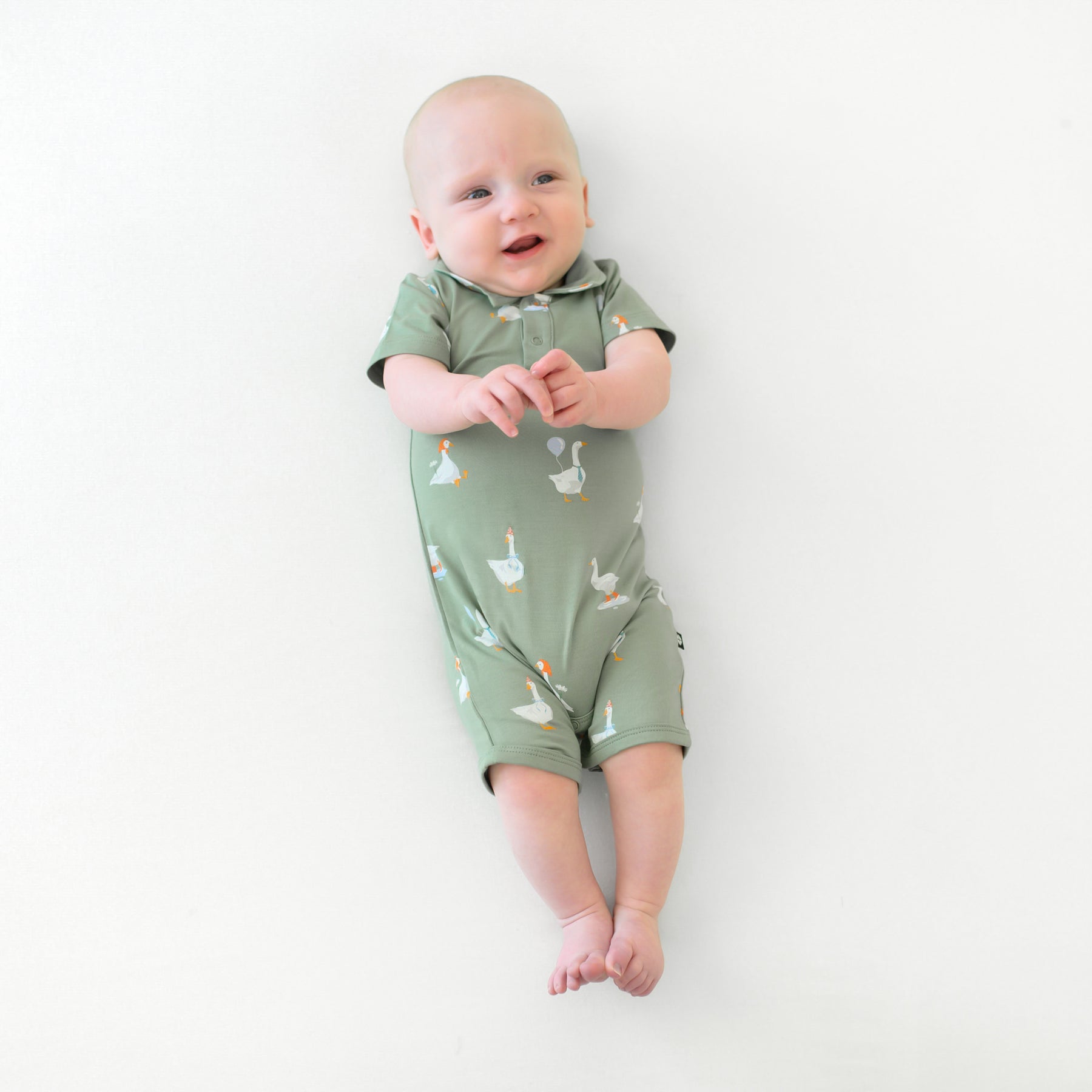 Infant laying down with his hands clasped in front of him wearing the Polo Shortall in Silly Goose