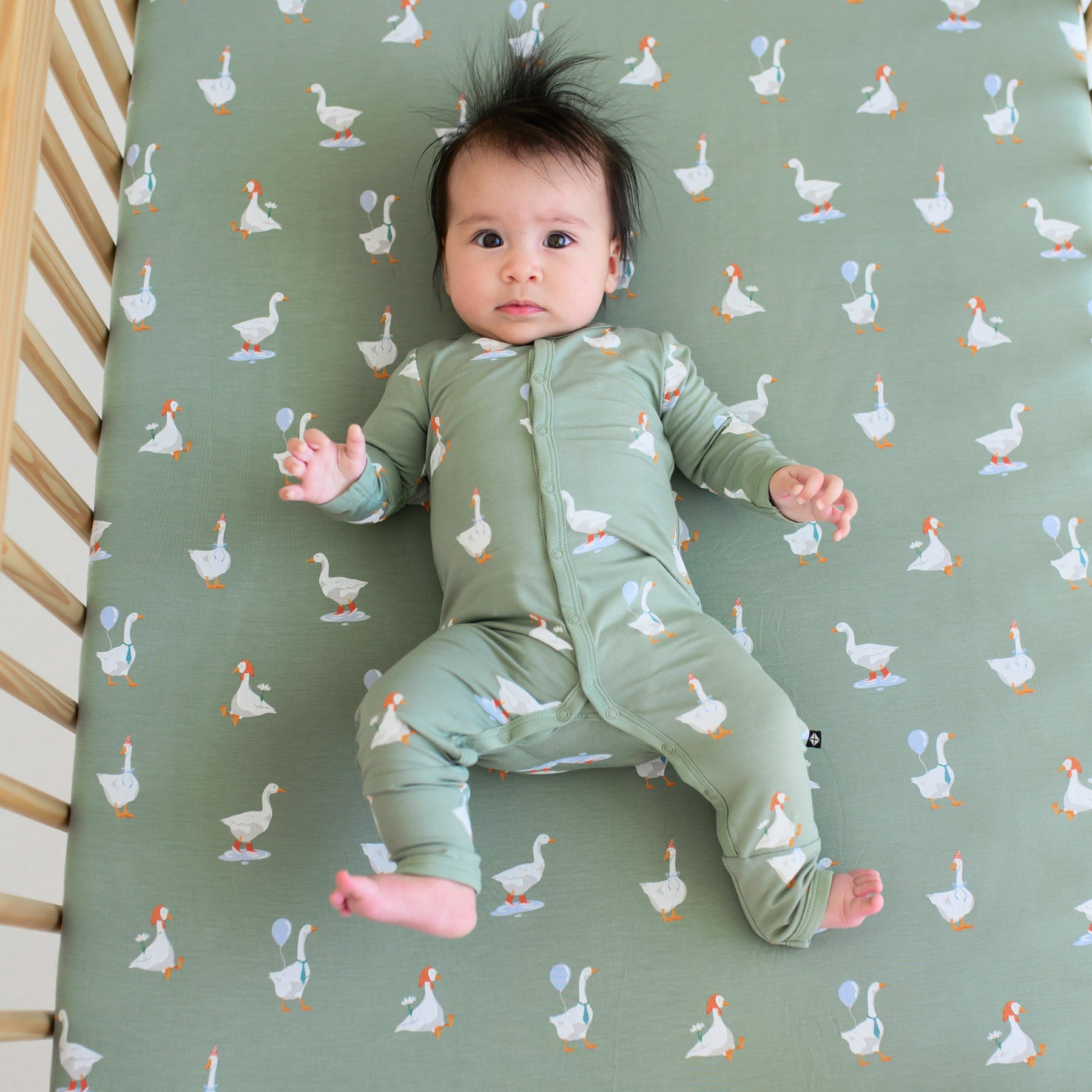 Infant laying in a crib on a Silly Goose Crib Sheet wearing matching snap Romper pajamas