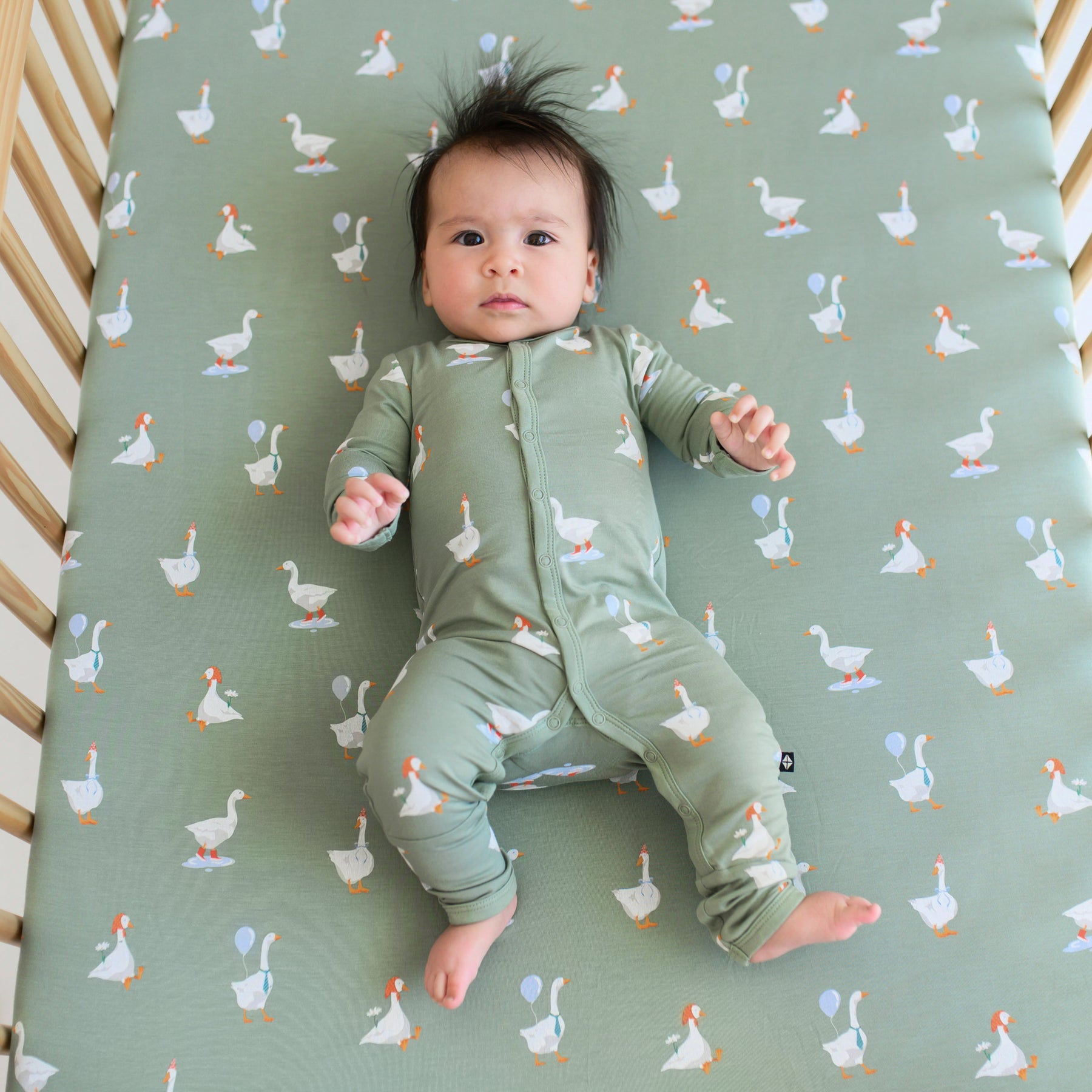 Infant wearing Silly Goose snap romper laying on matching goose crib sheet