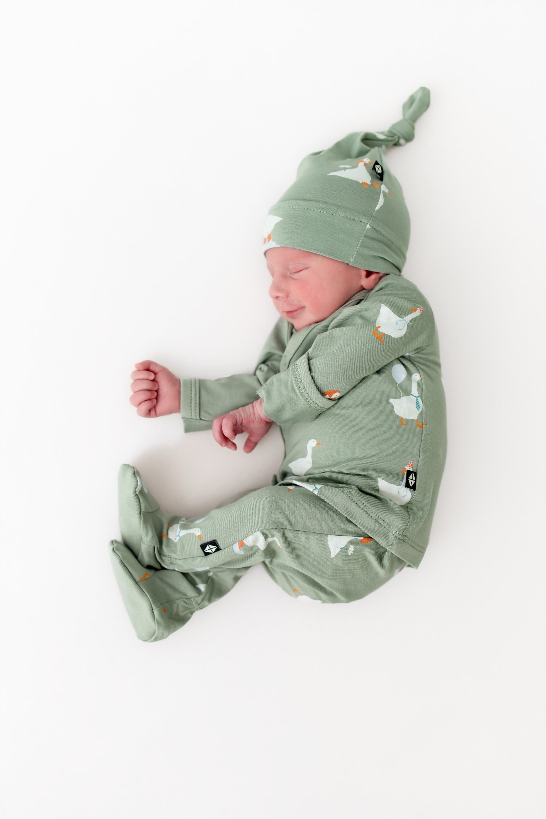 Newborn baby in a green outfit with silly goose pattern on a white background