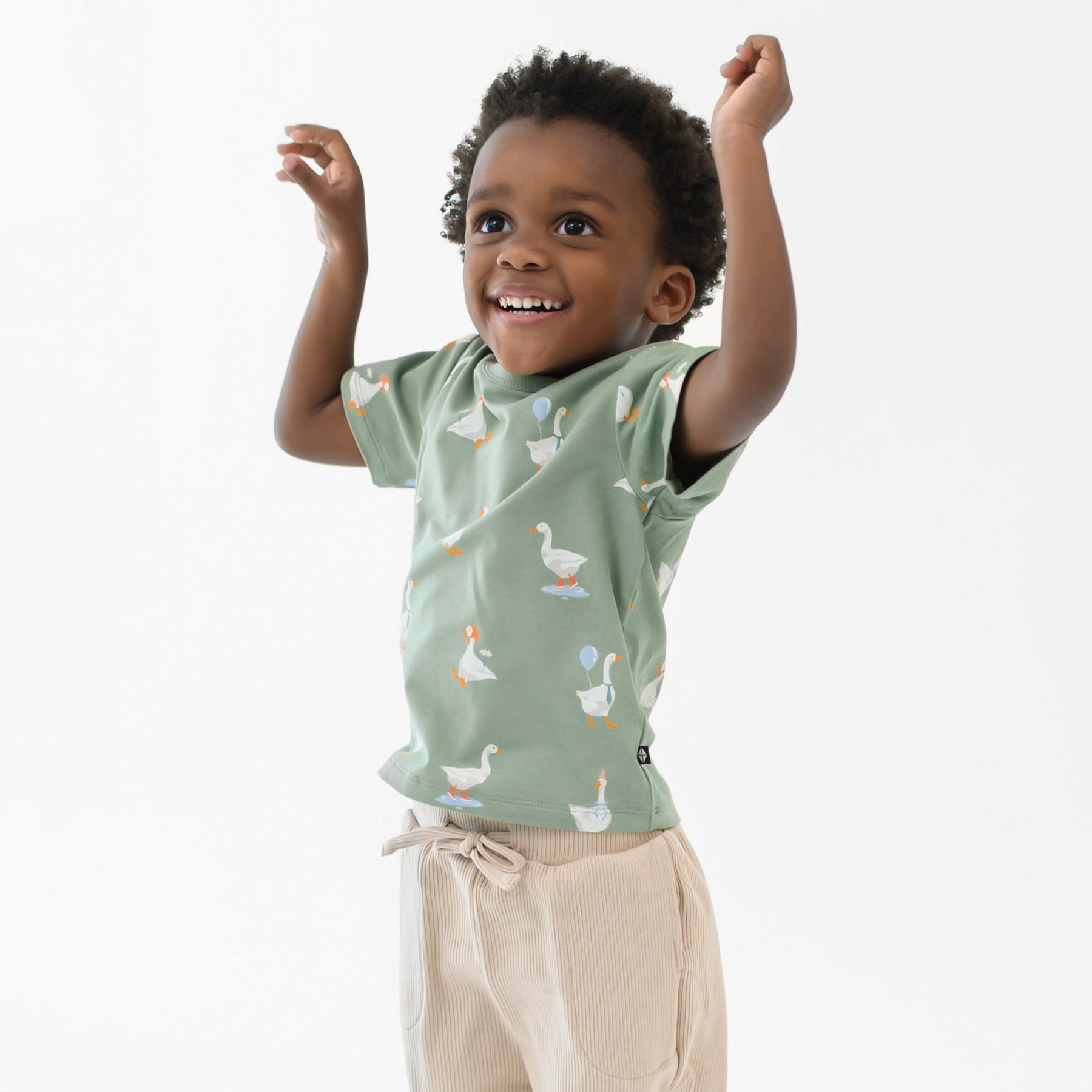 Young boy smiling with his arms in the air wearing the Toddler Basic Tee in Silly Goose and Bisque Ribbed Jogger Pants
