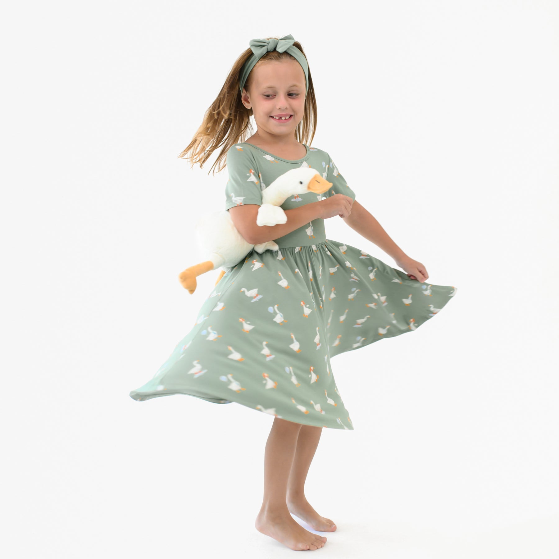 Young girl twirling in the Twirl Dress in Silly Goose holding a toy stuffed goose