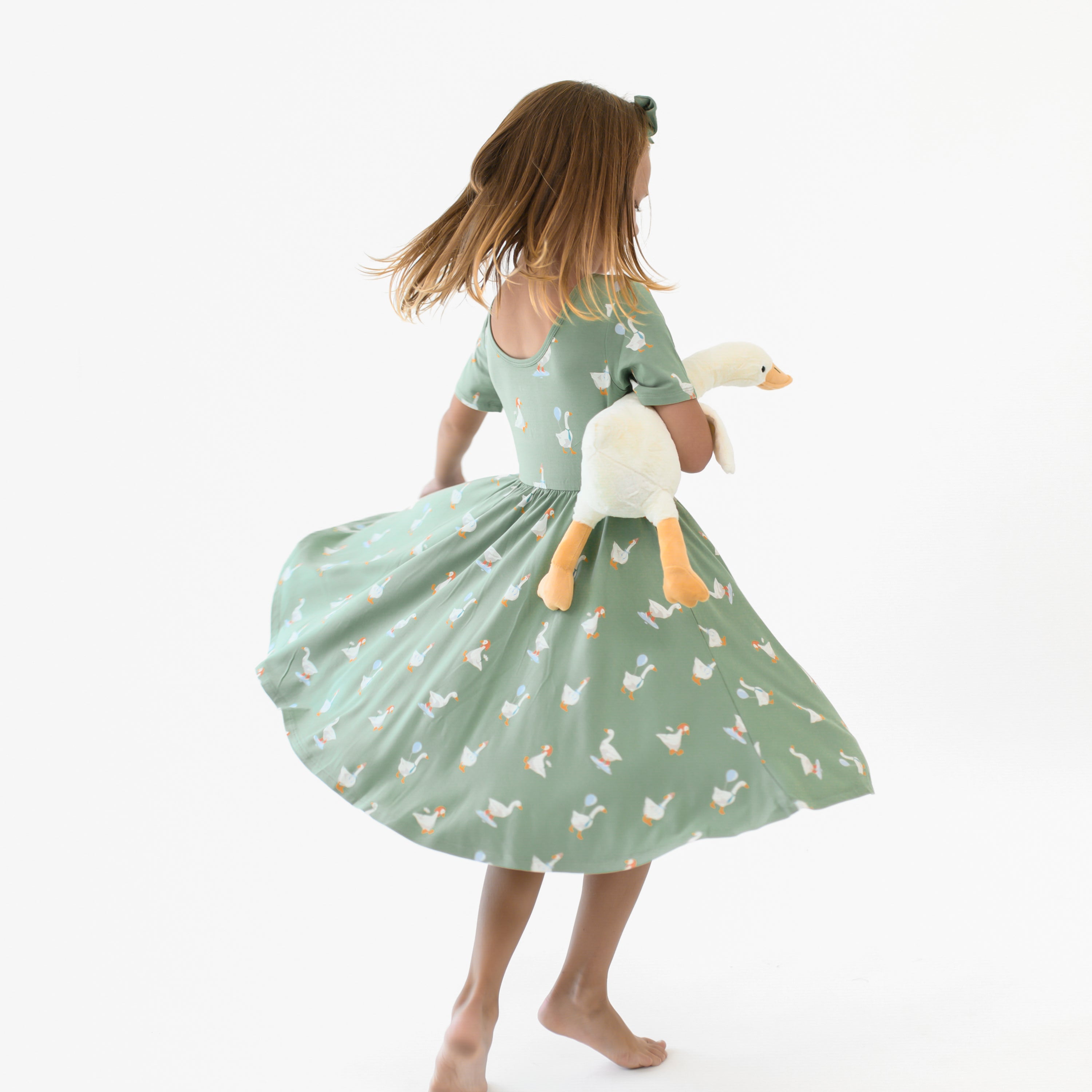 The ballerina neckline of the Twirl Dress in Silly Goose shown on a twirling model holding a toy stuffed goose