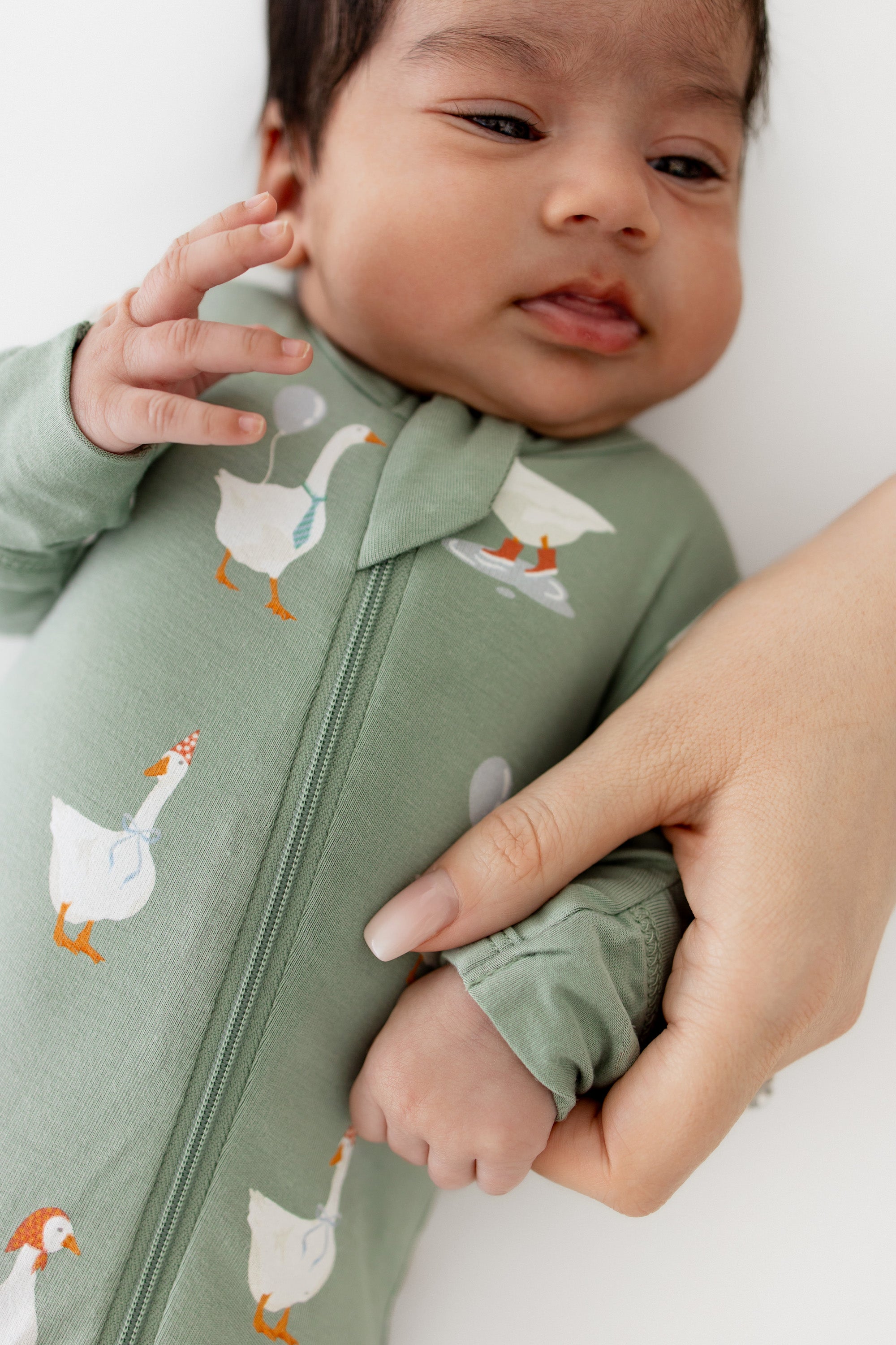 Baby wearing a green footie pajama with goose patterns, held by an adult hand.