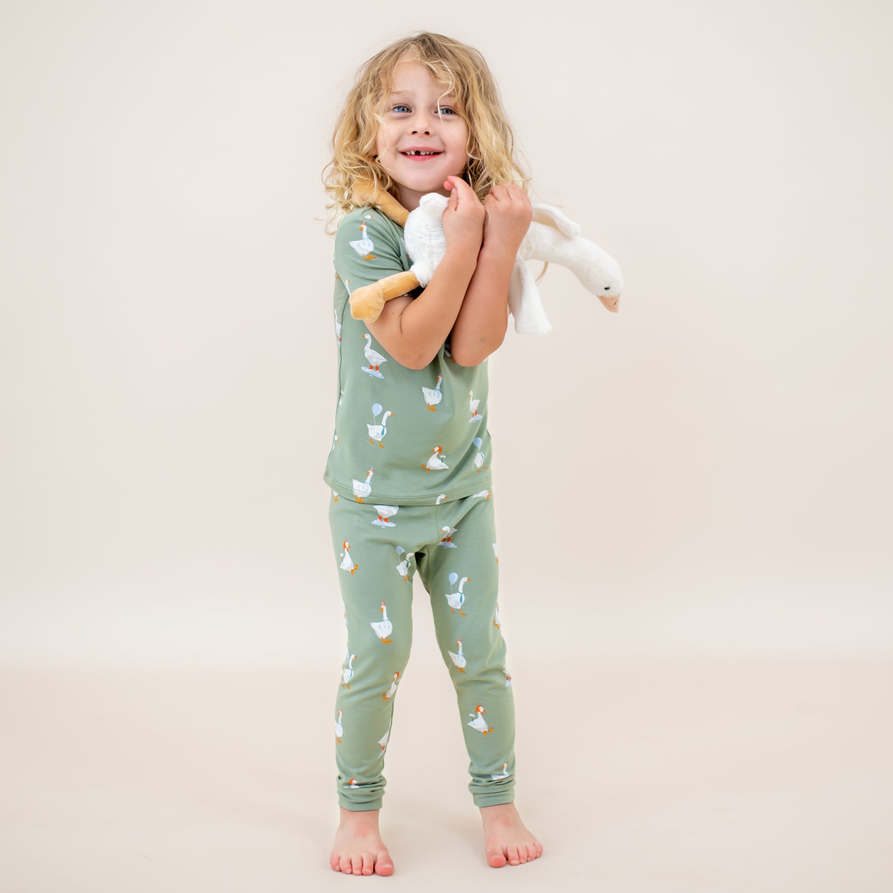 Young child standing holding a stuffed toy goose in front of them wearing the Short Sleeve with Pants Pajamas in Silly Goose