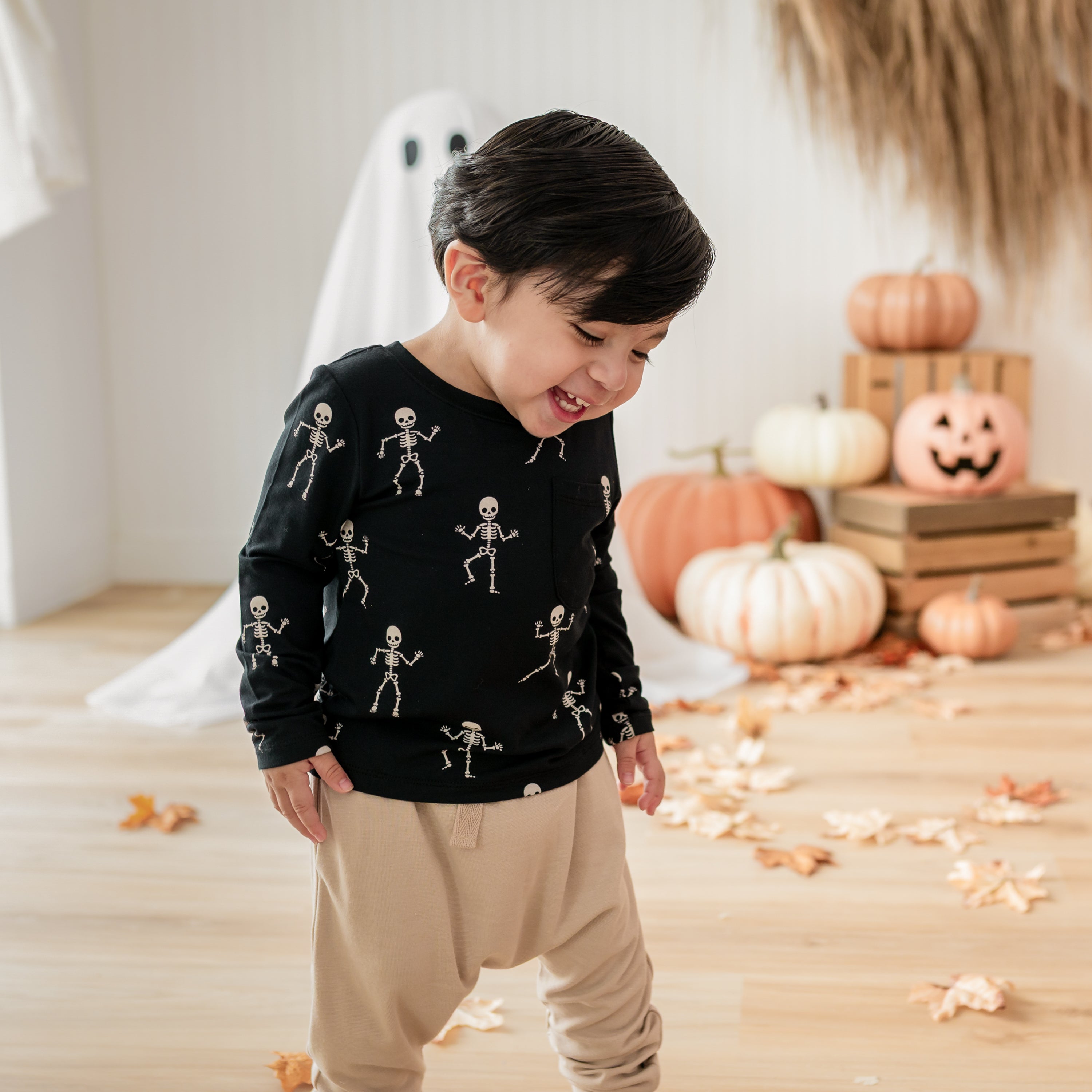 Laughing toddler walking wearing the Long Sleeve Toddler Crew Neck Tee in Skeleton in front of a fall backdrop