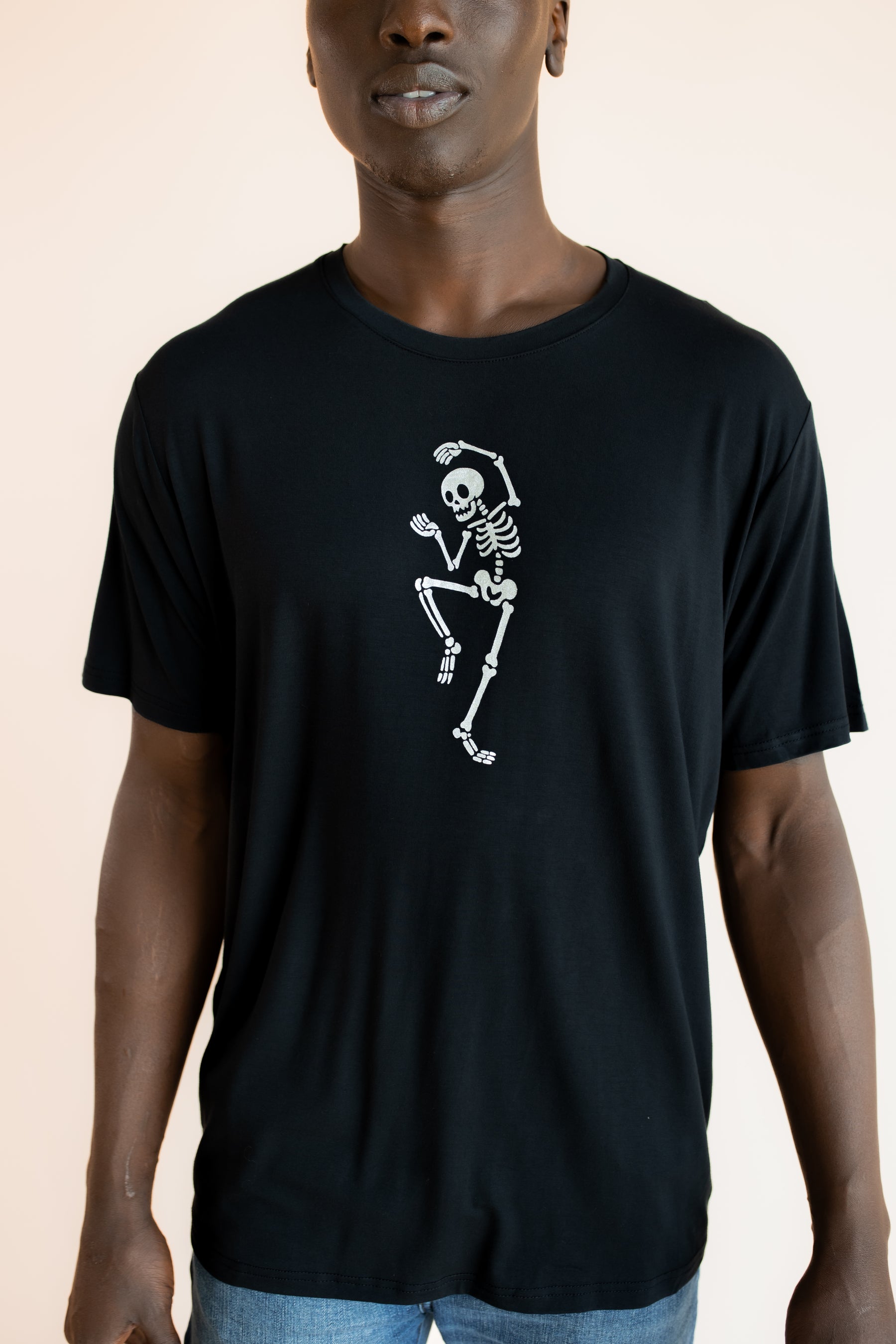 Close up of Modal wearing Black Men's Crew Neck Tee with Skeleton print in center on a beige background
