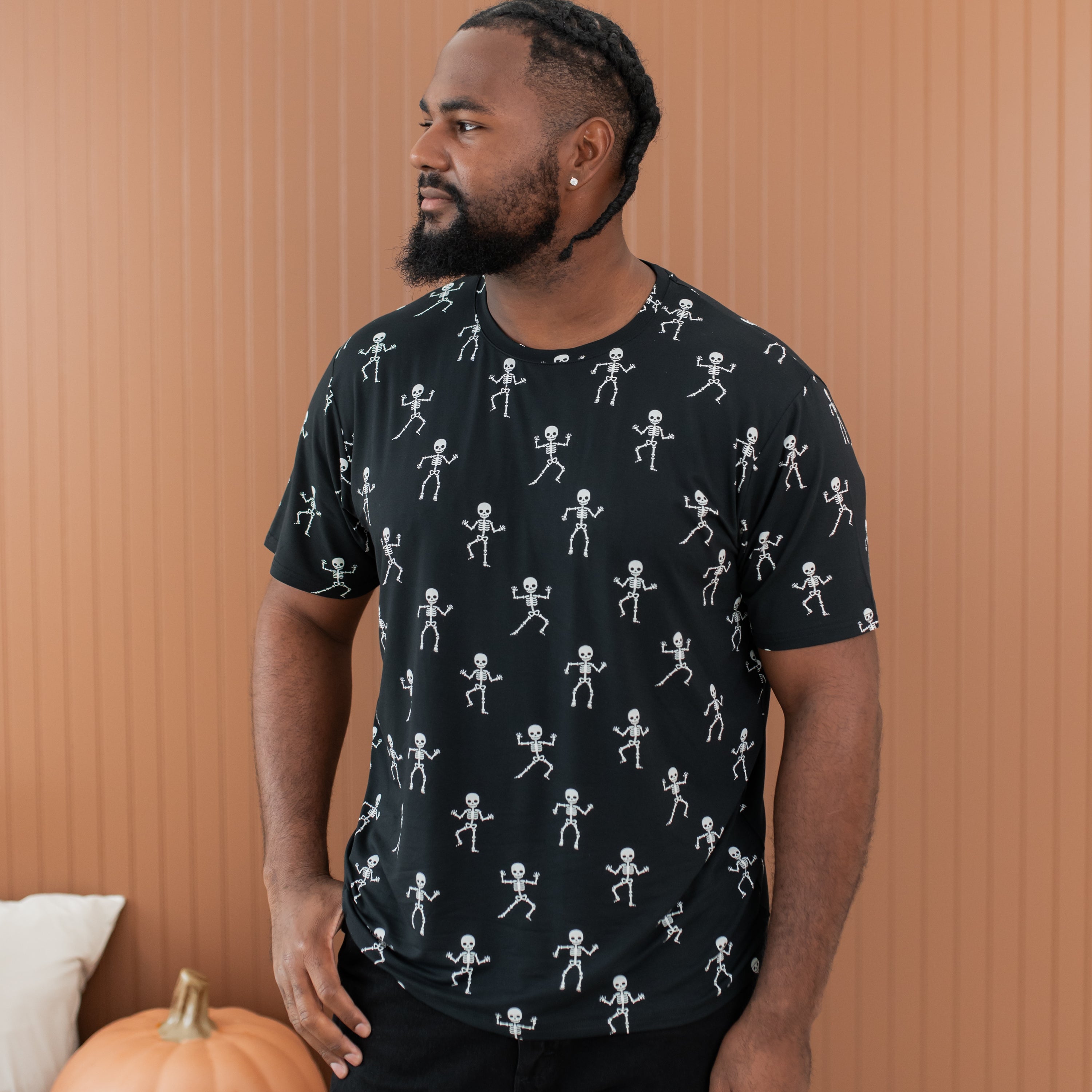 Man wearing a black t-shirt with white skeleton patterns against a brown wall.