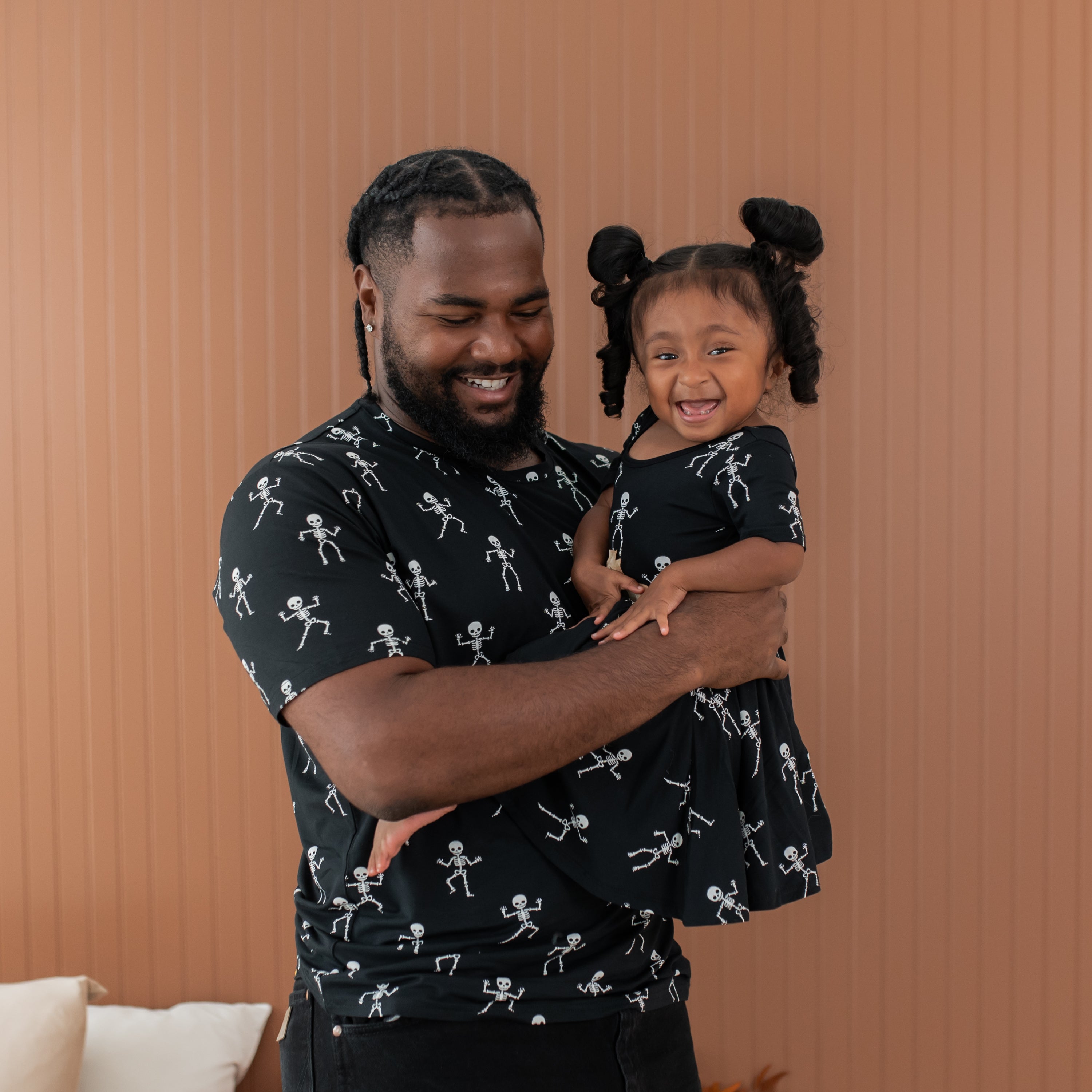 Man and young girl wearing matching black shirts with white skeleton pattern against a brown background