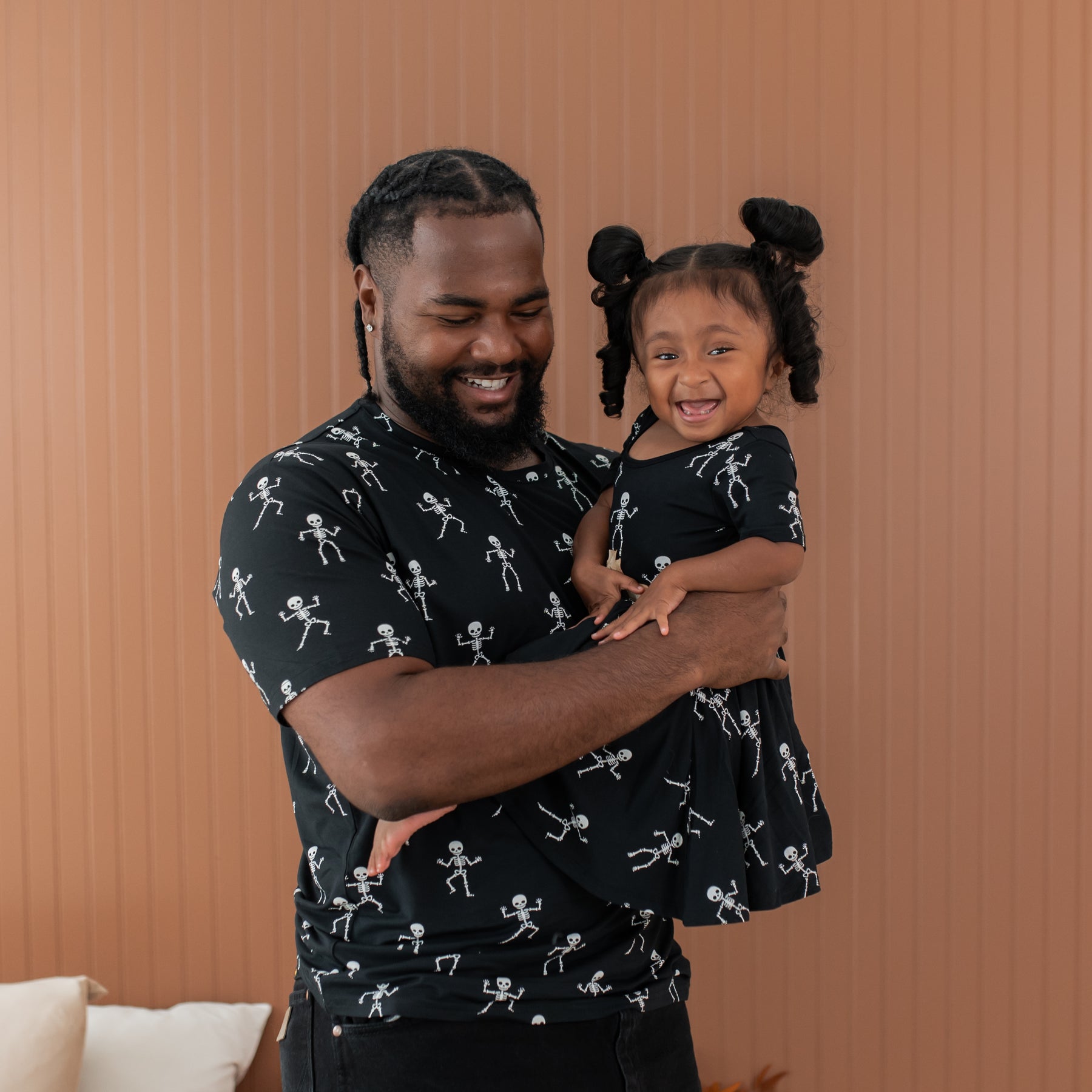 Man and young girl wearing matching black shirts with white skeleton pattern against a brown background
