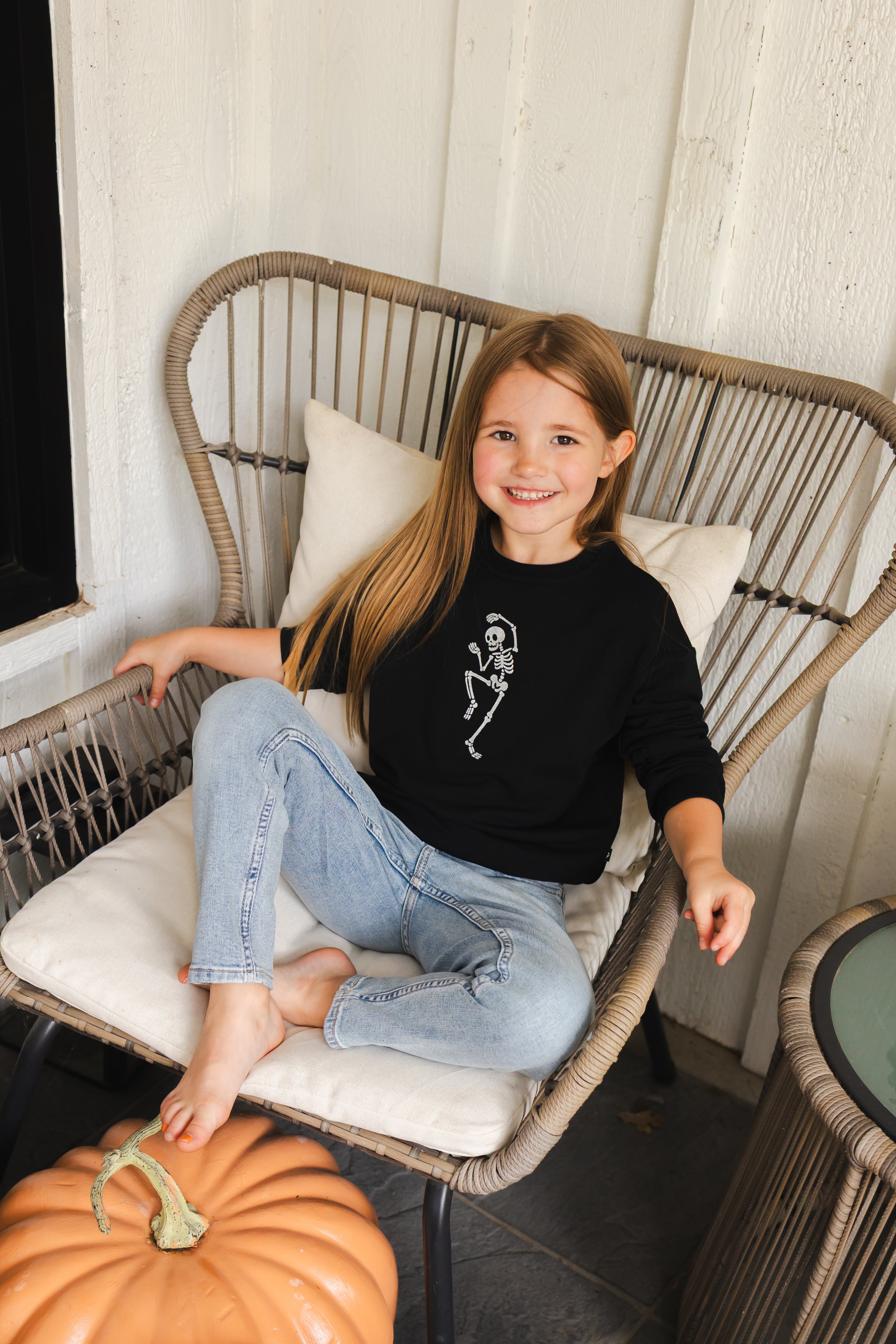 Girl wearing Black Sweatshirt with Skeleton print in the center sitting on a chair