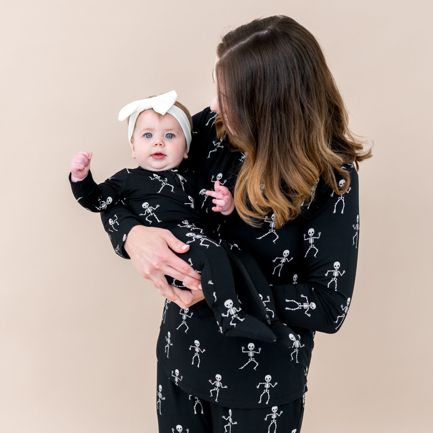 Mom wearing Women's jogger set holding daughter in matching Mommy and Me pajamas in Skeleton Halloween print