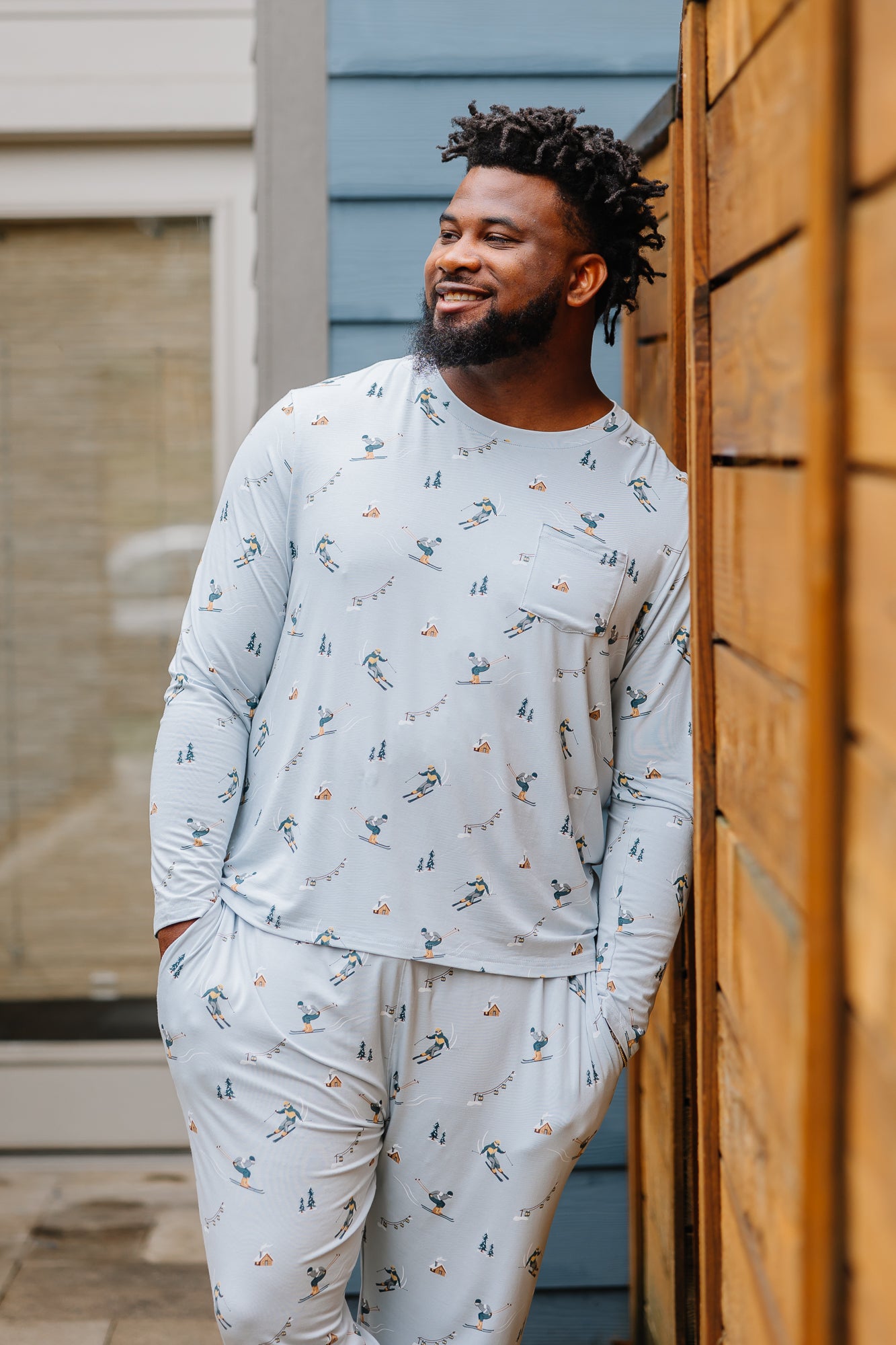 Smiling male model wearing the Men's Jogger Set in Ski looking off to the side leaning up against a fence 