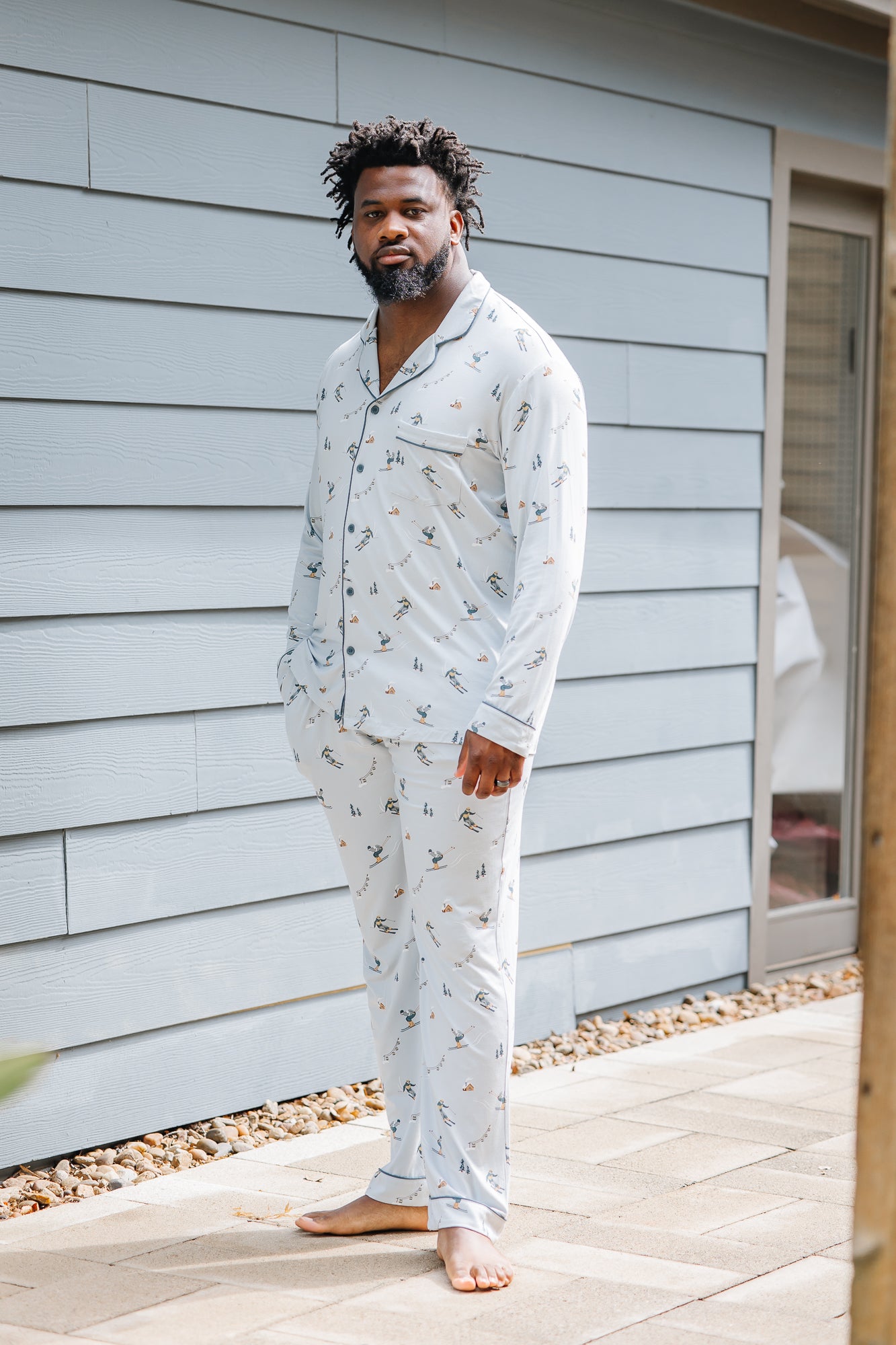 Male model standing in front of a house wearing the Men's Long Sleeve Pajama Set in Ski with one hand in the pants pocket