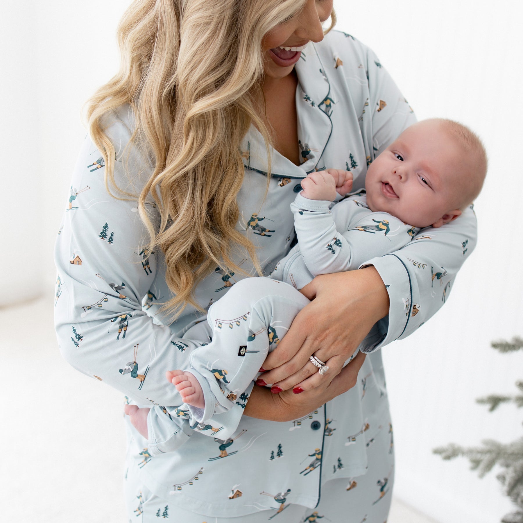 Mother wearing the long sleeve women's pajama set in ski holding her infant on who is matching in a Zippered Romper in Ski