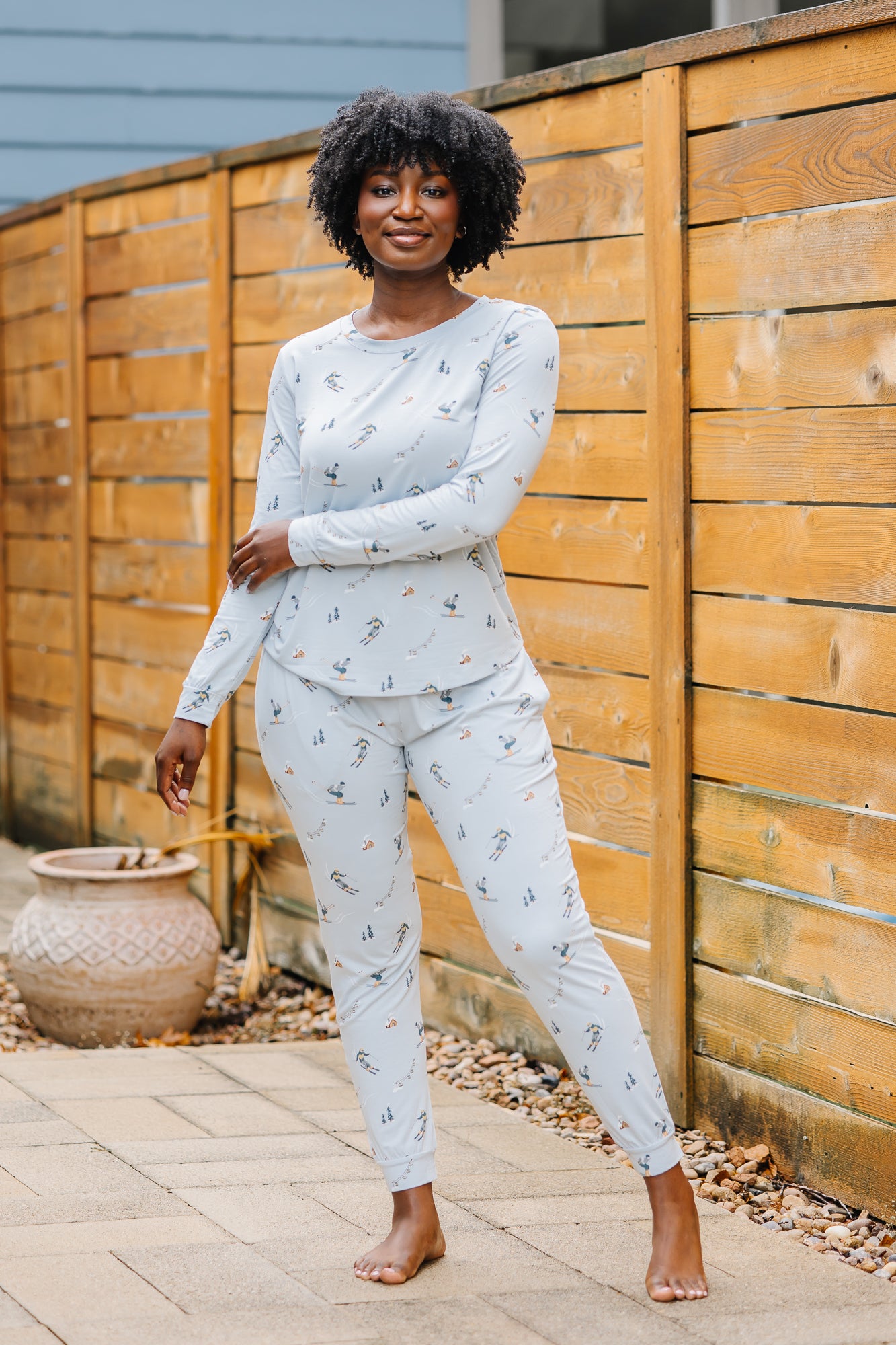 Smiling model wearing the Women's Jogger Pajama Set in Ski standing beside a wooden fence