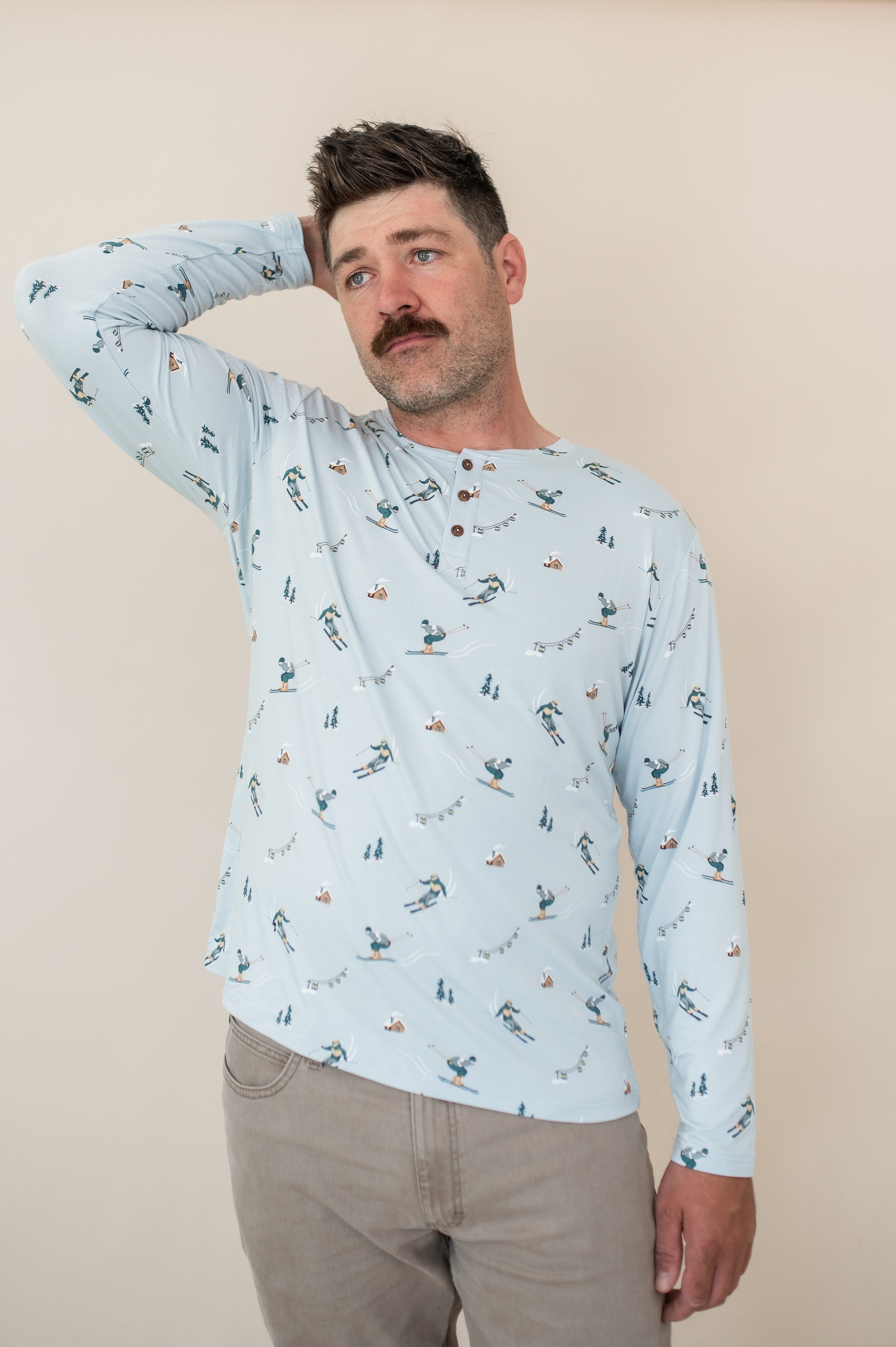 Male modeling the Men's Long Sleeve Henley Top in Ski looking off to the side with one hand up behind his head