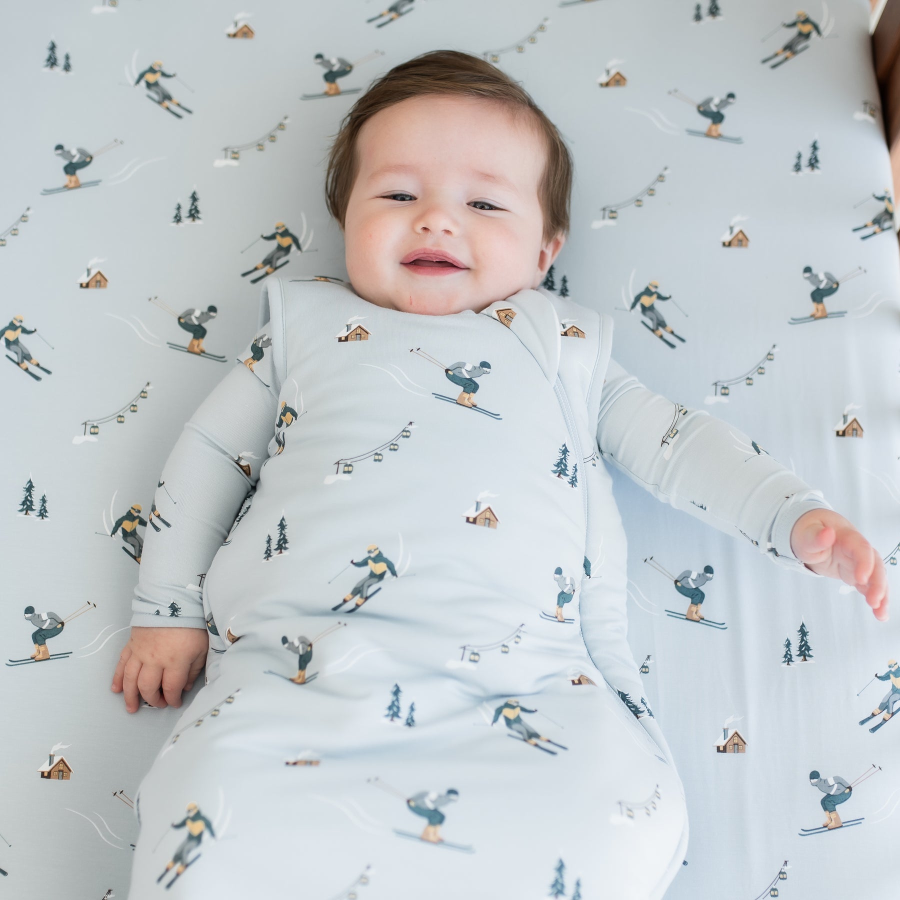 Close up of infant laying in a crib on a Crib Sheet in Ski wearing a matching sleep bag and romper