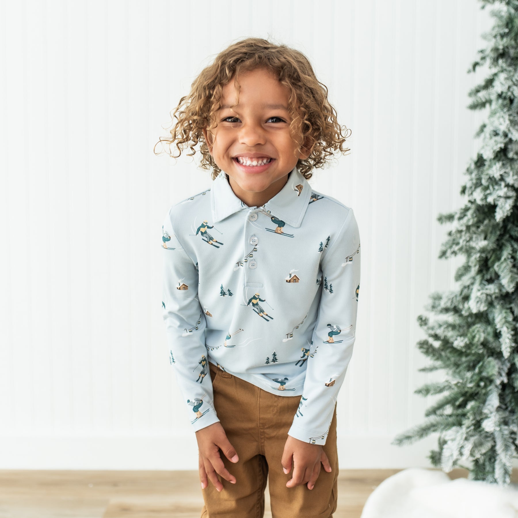 Smiling boy wearing the Toddler Long Sleeve Polo in Ski with bronze colored pants