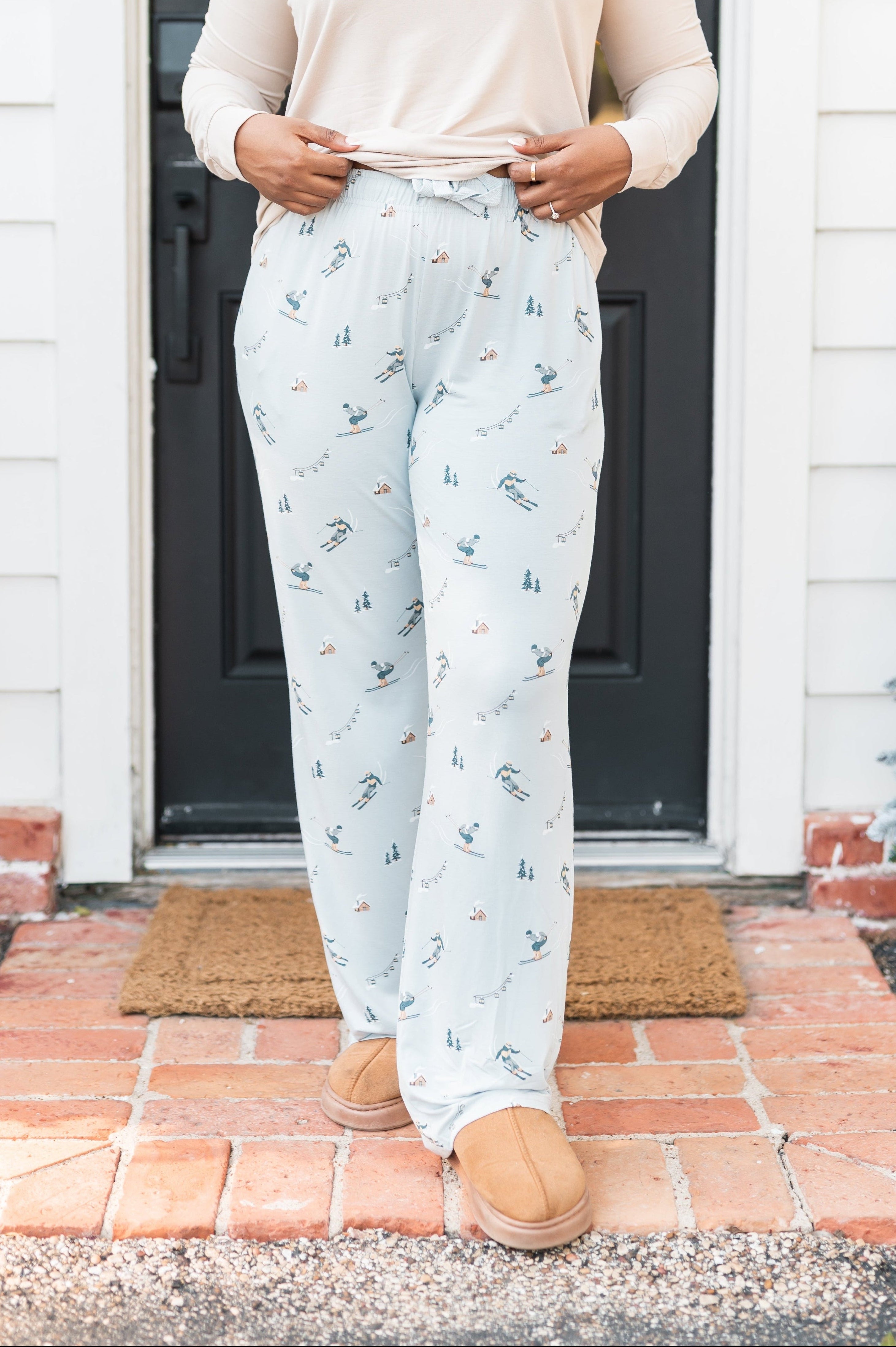 Female standing at a front door wearing the Women's Lounge Pants in Ski with a cream colored shirt and atlantic beanie