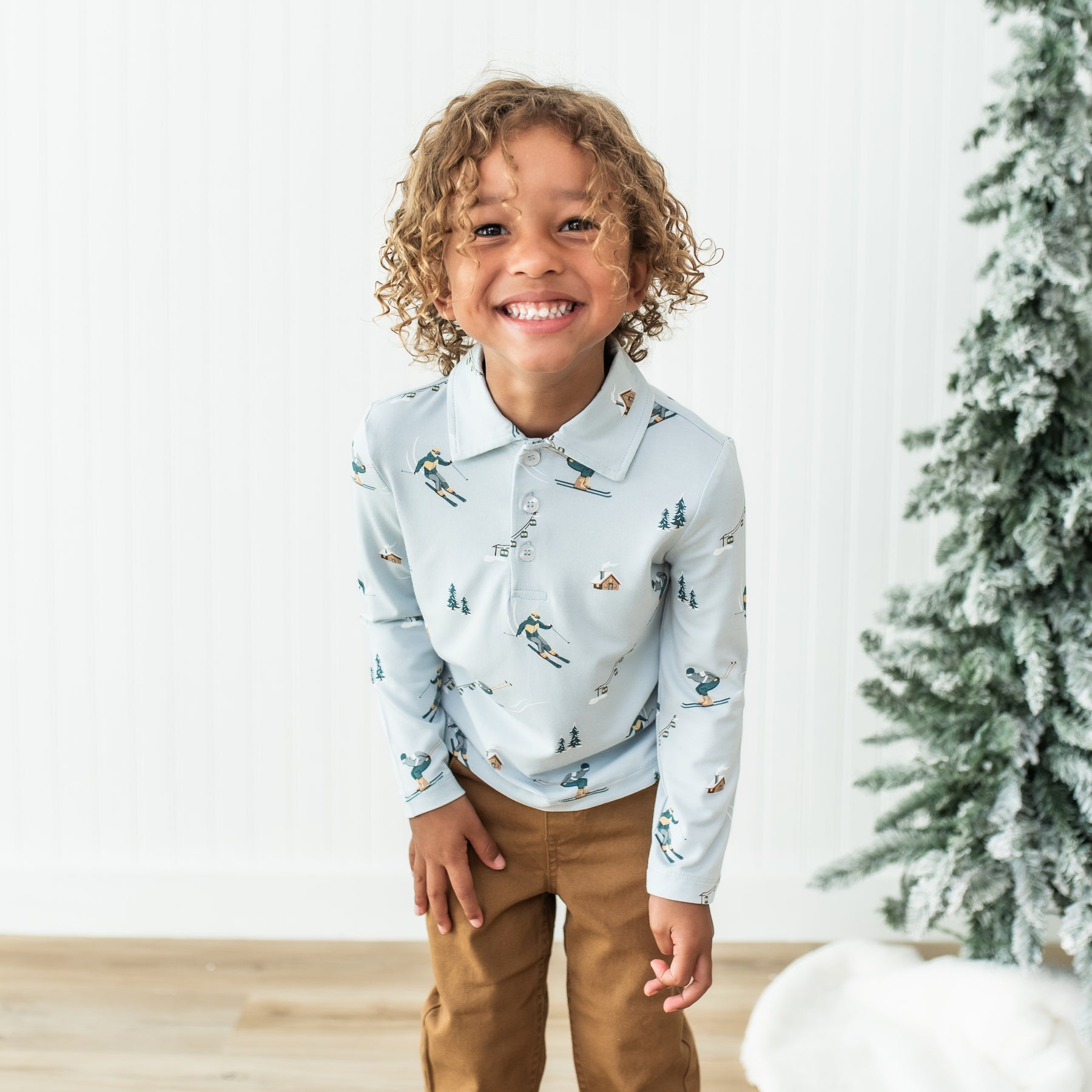 Smiling young boy wearing the Toddler Long Sleeve Polo in Ski with bronze colored pants