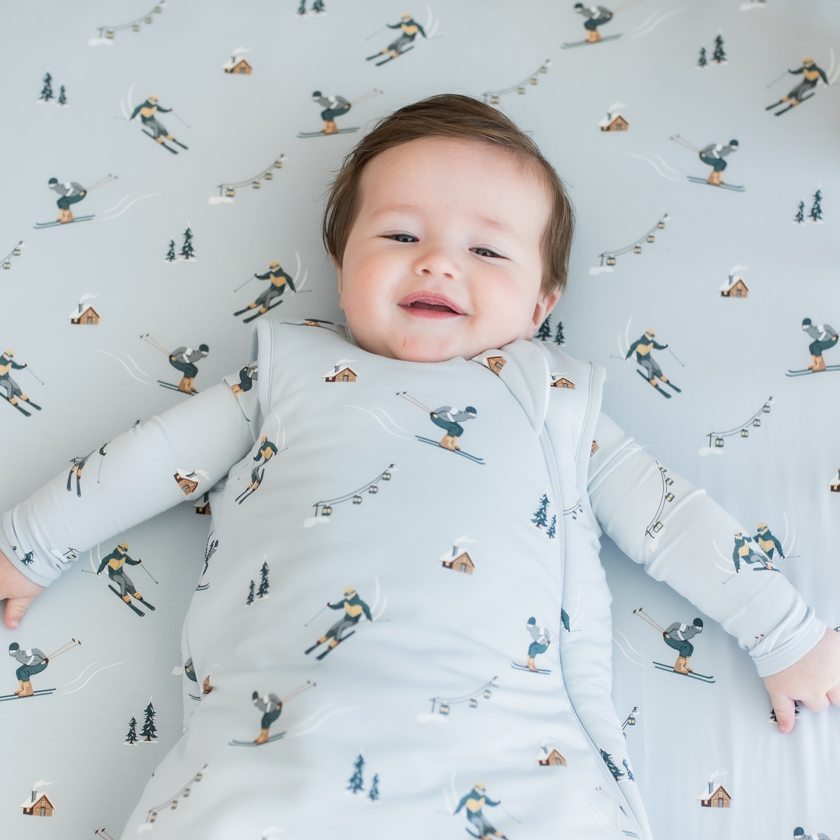 Close up of an infant wearing the Sleep Bag in Ski 2.5 laying on a matching crib sheet