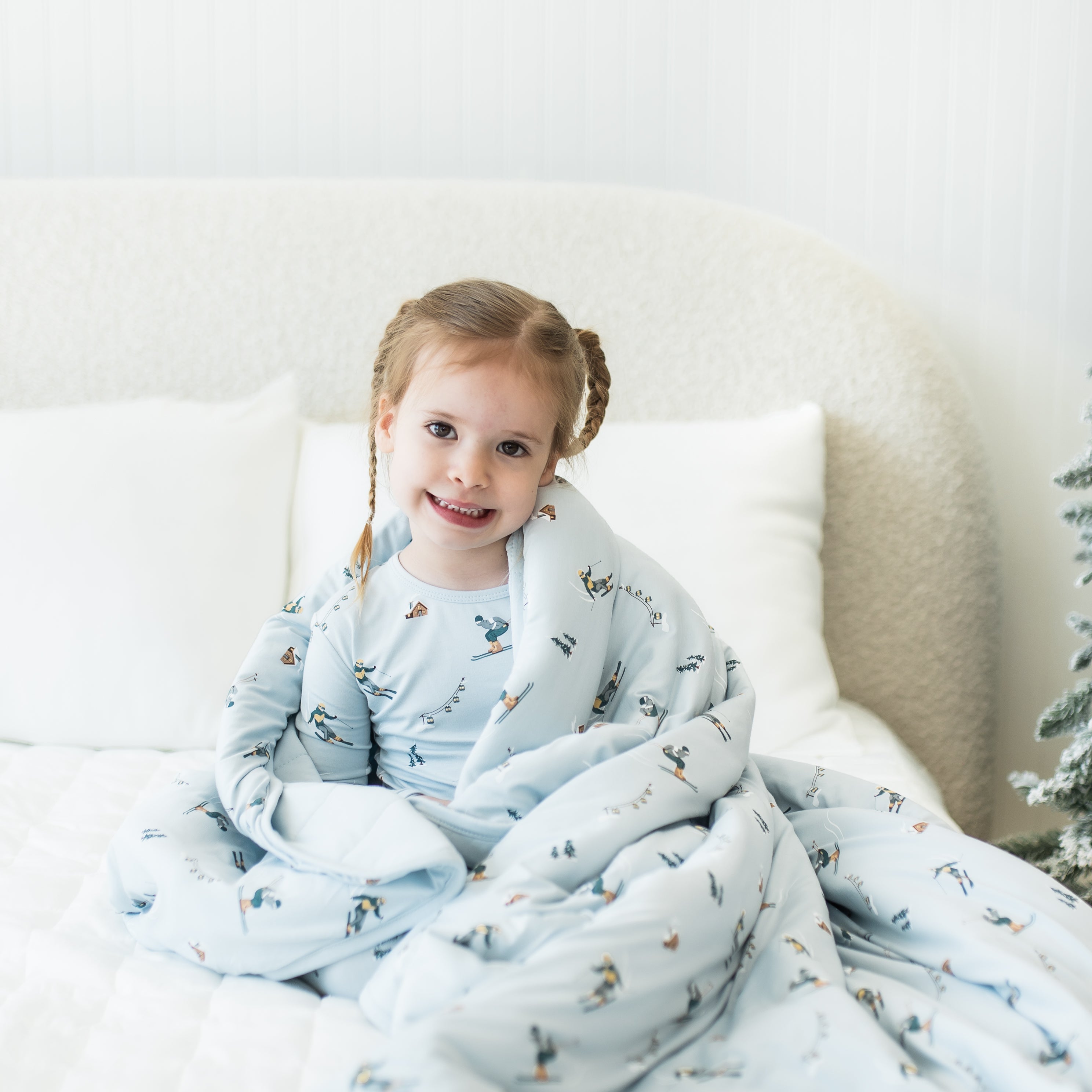 Young girl sitting on a bed with the Youth Blanket in Ski 2.5 wrapped around her