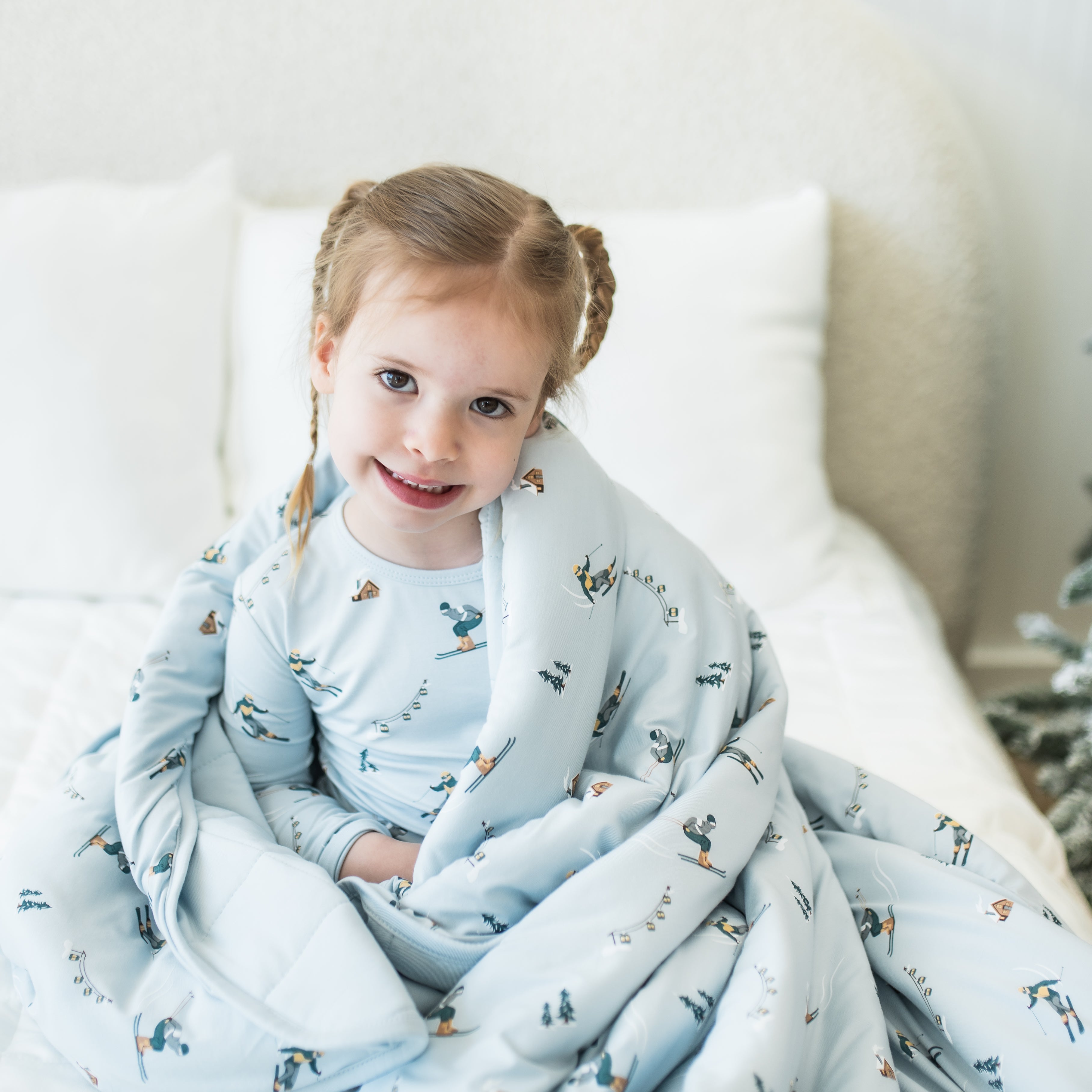 Close up of young girl sitting on a bed with the Youth Blanket in Ski 2.5 wrapped around her