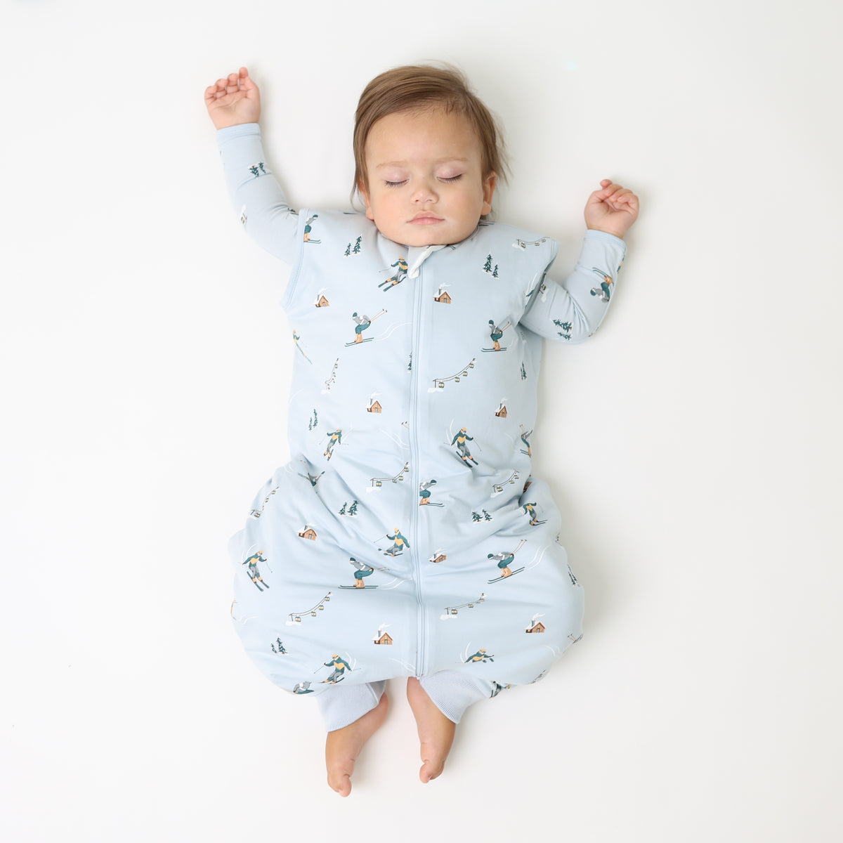 Toddler laying on a light neutral surface wearing the Sleep Bag Walker in Ski 1.0 with a matching long sleeve romper on underneath