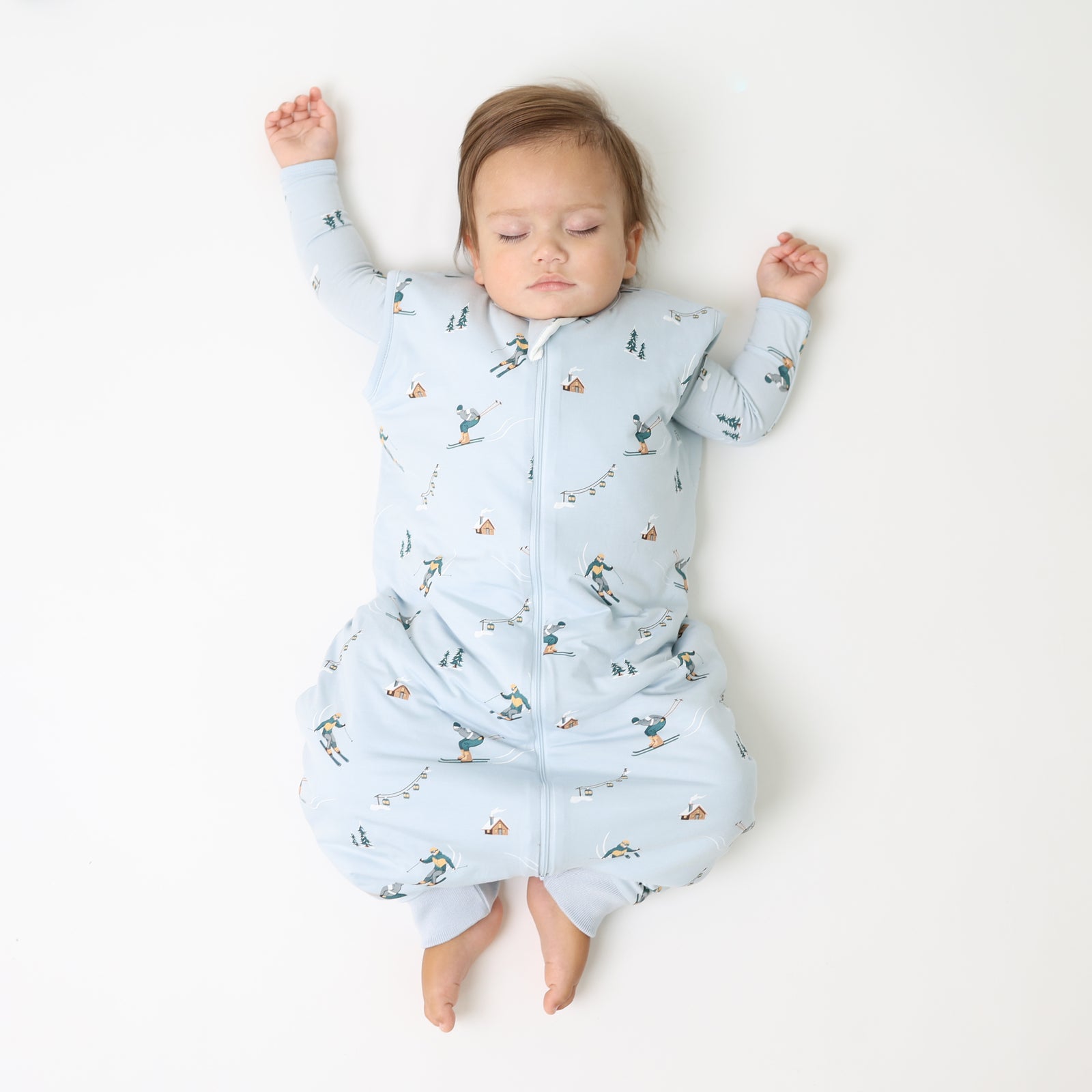 Toddler laying on a light neutral surface wearing the Sleep Bag Walker in Ski 1.0 with a matching long sleeve romper on underneath