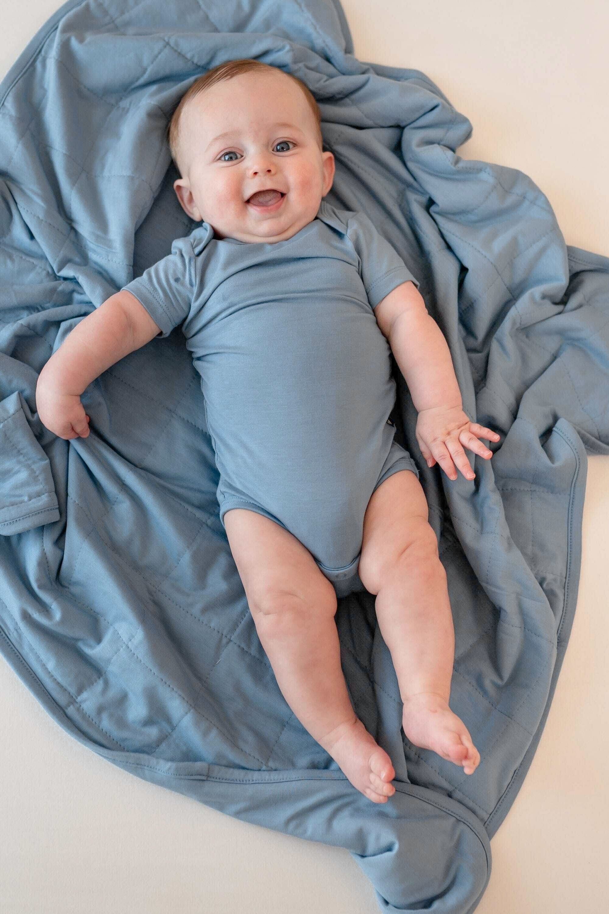 Baby in a blue bodysuit laying on a blue blanket