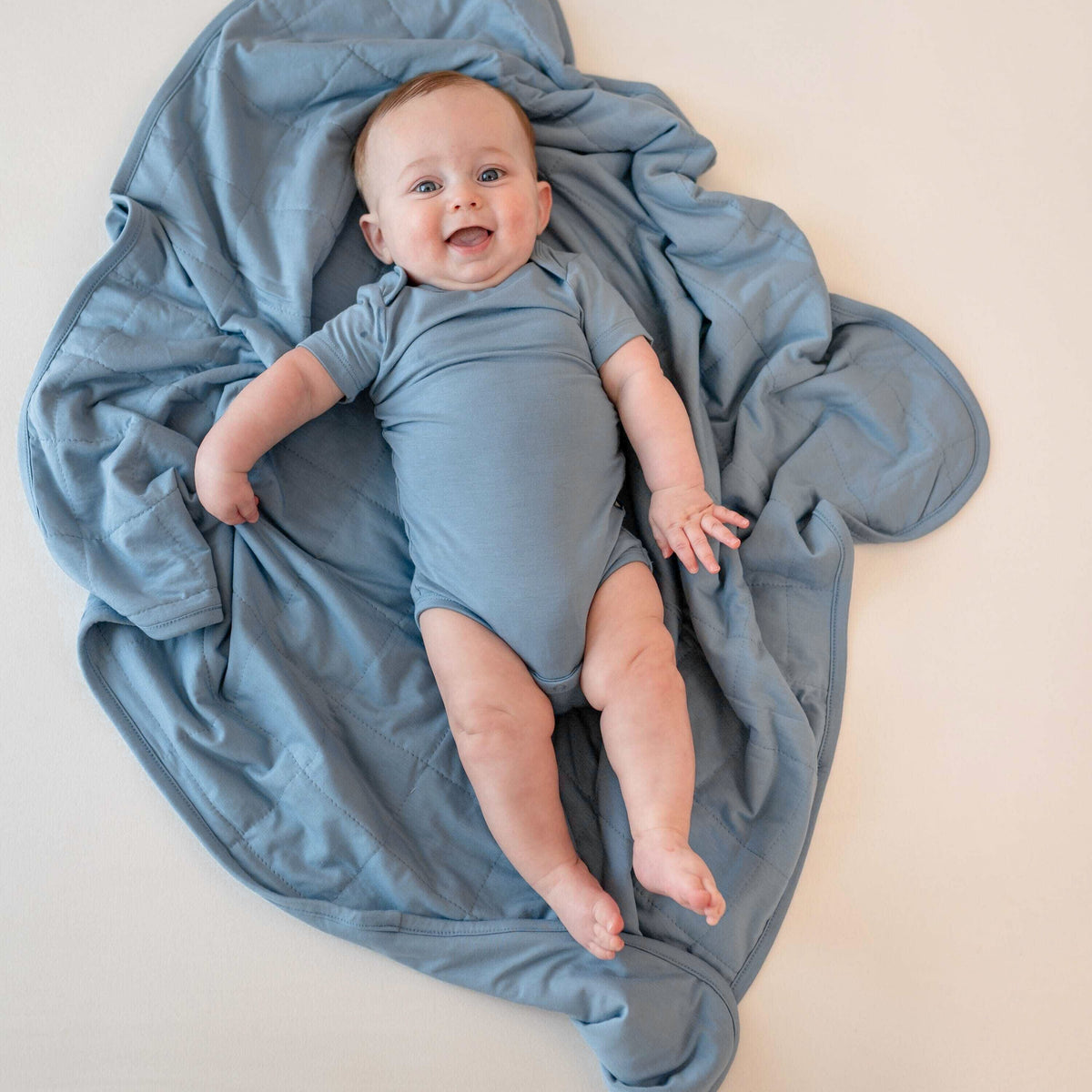 Baby in a blue bodysuit laying on a blue blanket