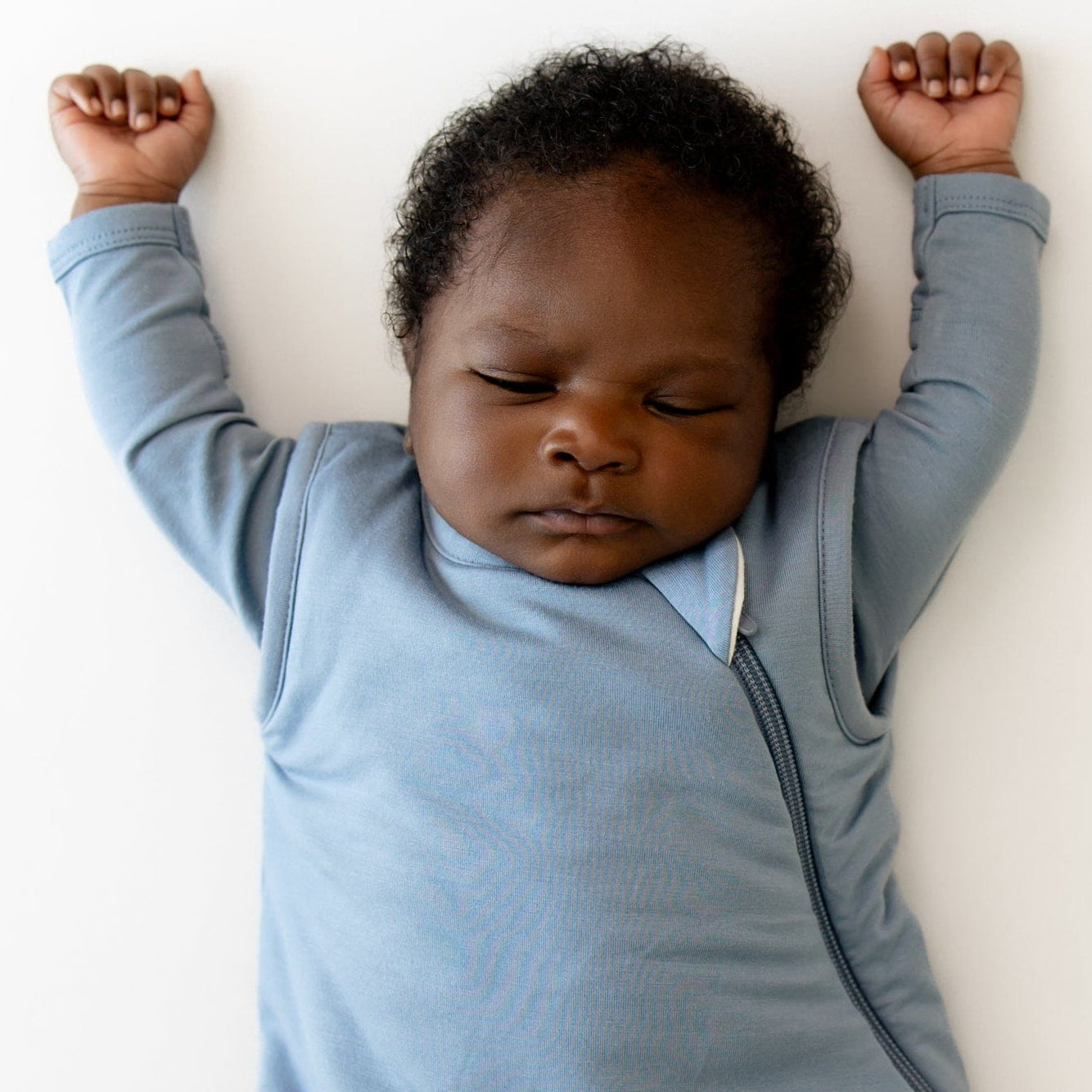 Baby in a blue sleep bag lying on a white surface