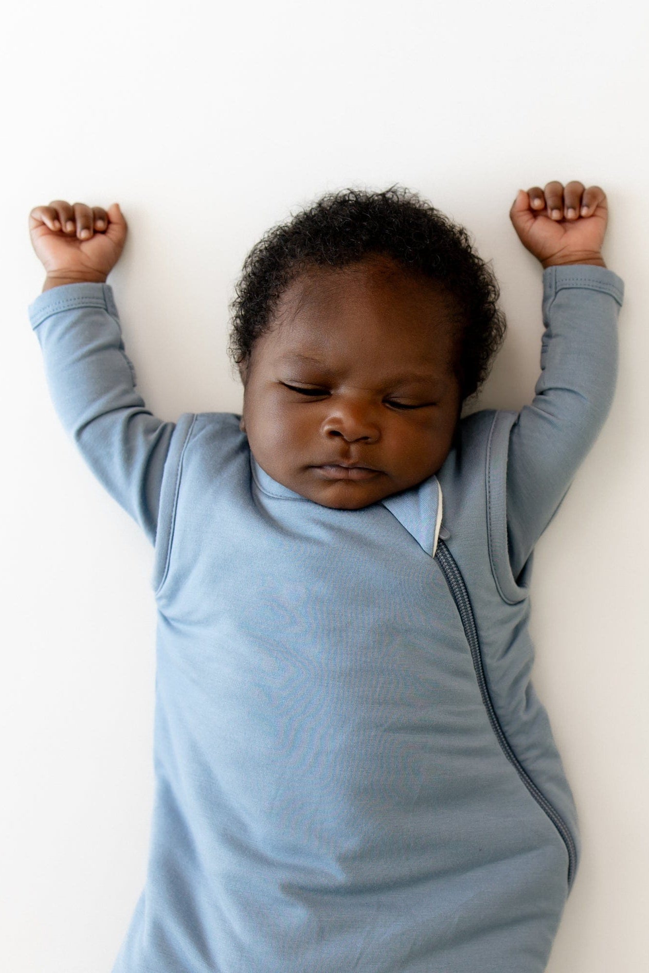 Baby in a blue sleep bag lying on a white surface