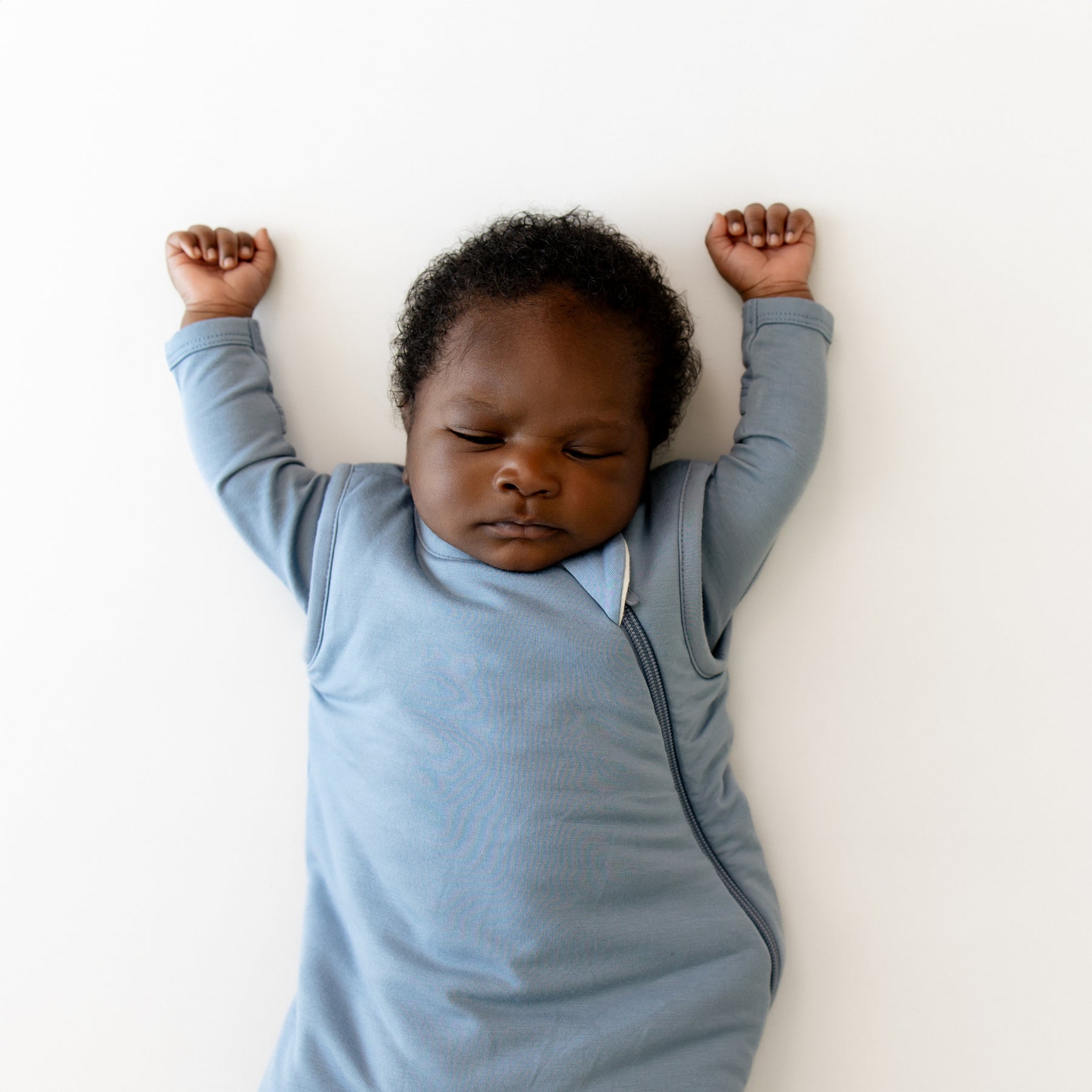 Baby in a blue sleep bag lying on a white surface