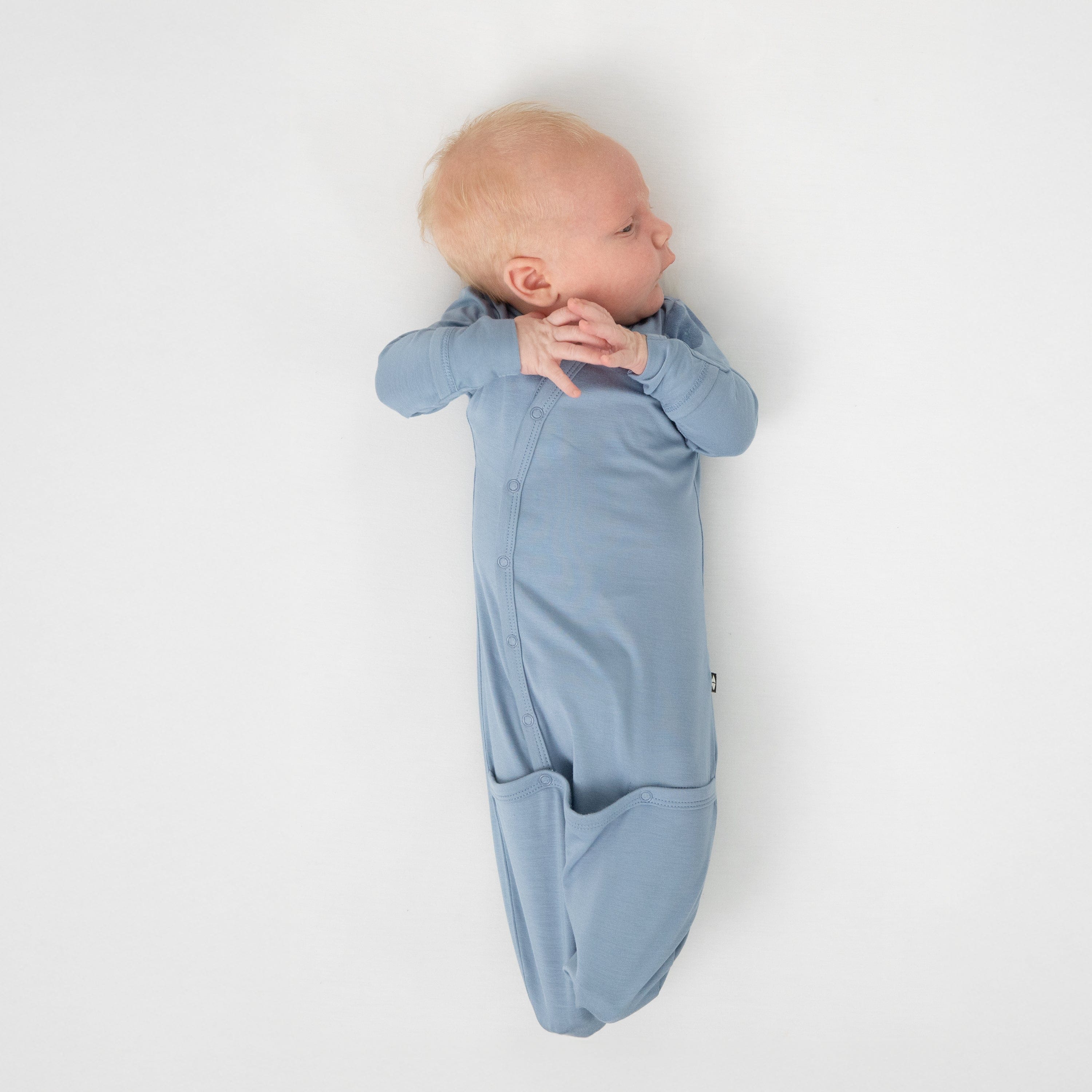 Newborn laying on a white blanket wearing the Bundler in Slate