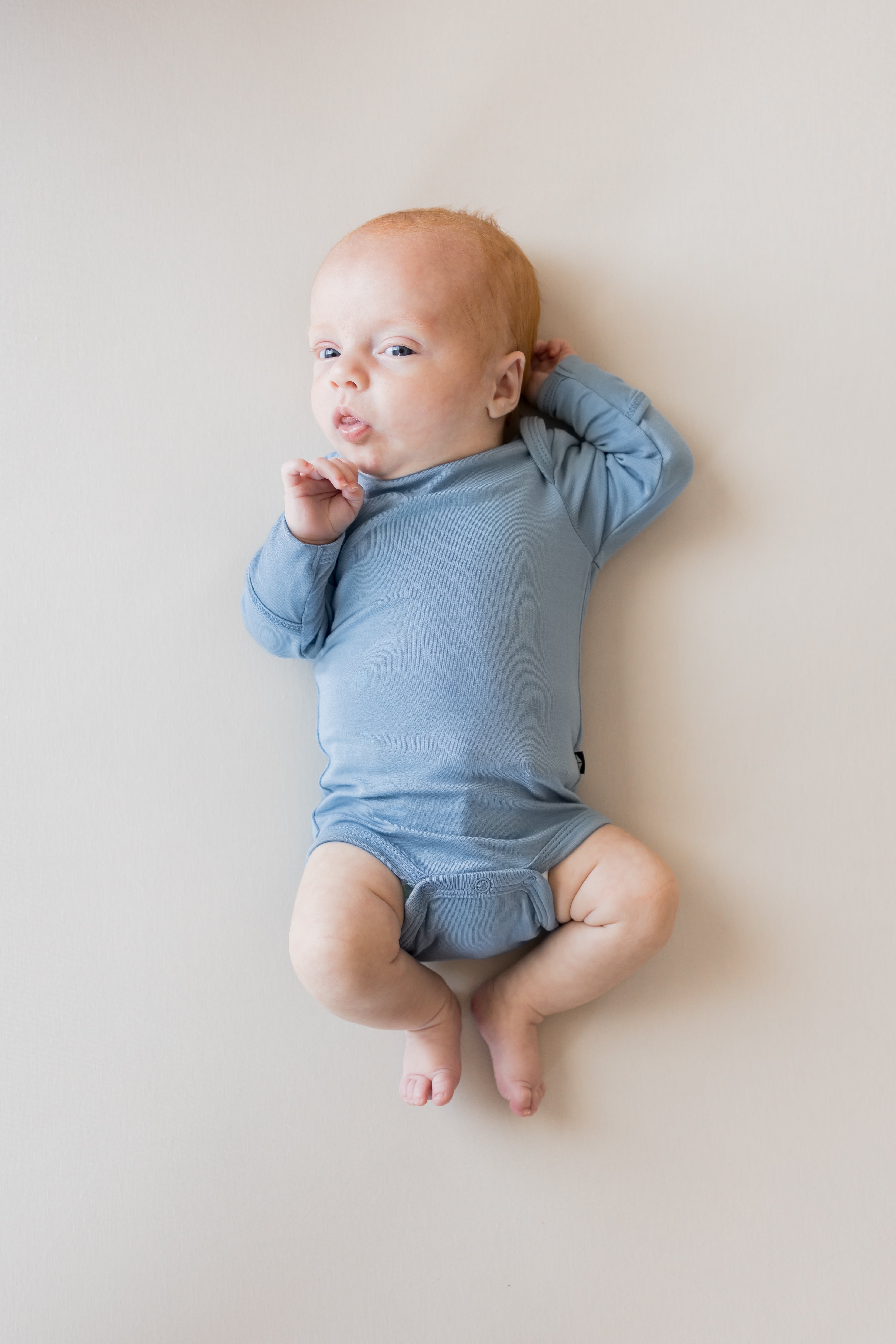 Baby wearing Long Sleeve Bodysuit in Slate color on a beige background
