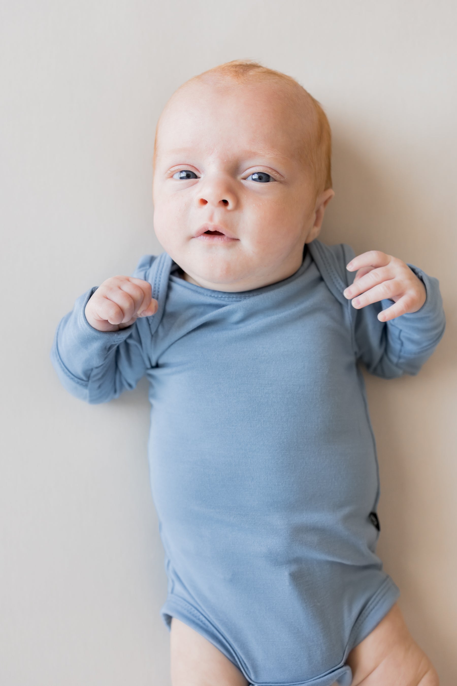 Close up of Baby wearing Long Sleeve Bodysuit in Slate color on a beige background