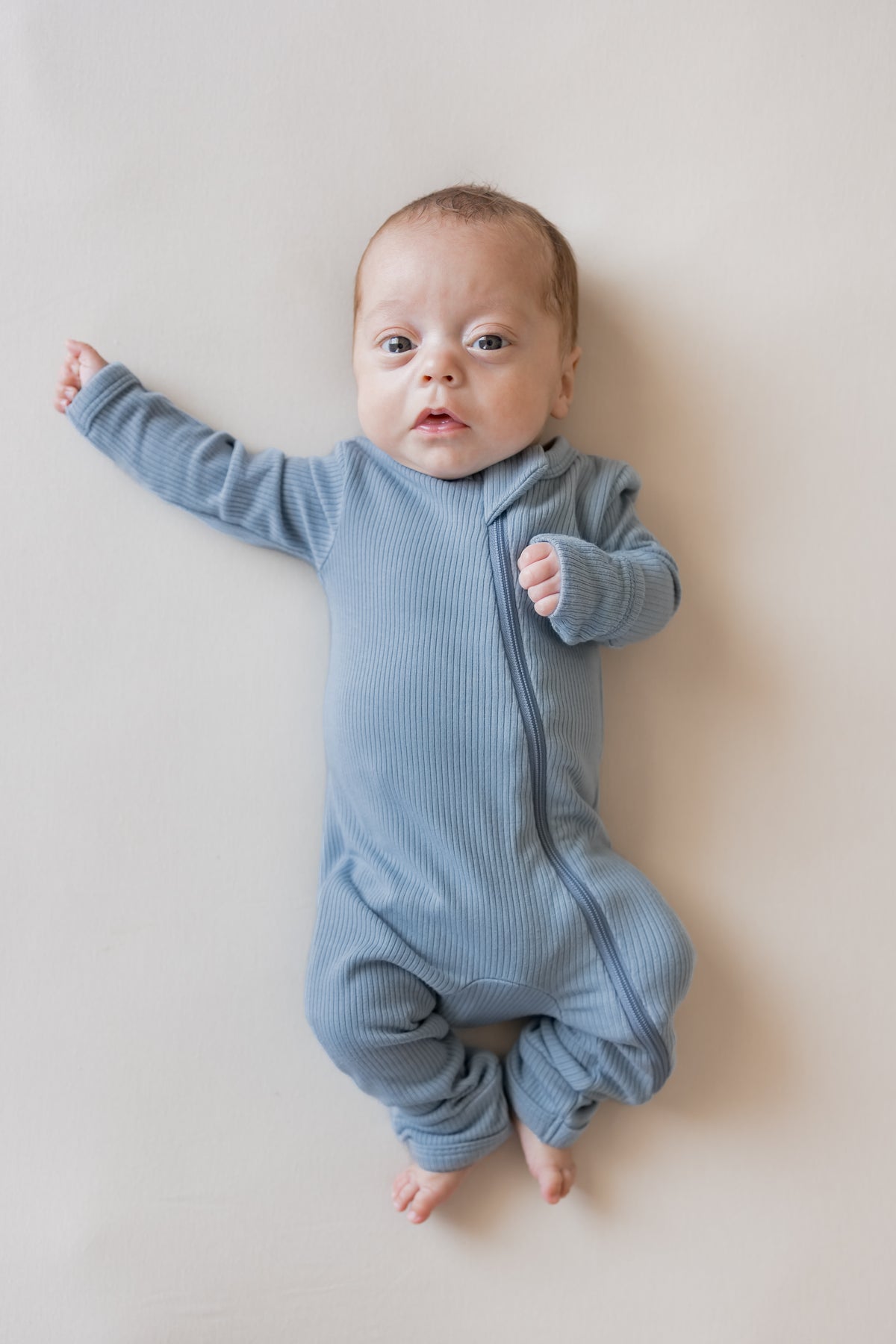 Baby wearing Ribbed Zippered Romper in Slate color on a beige background