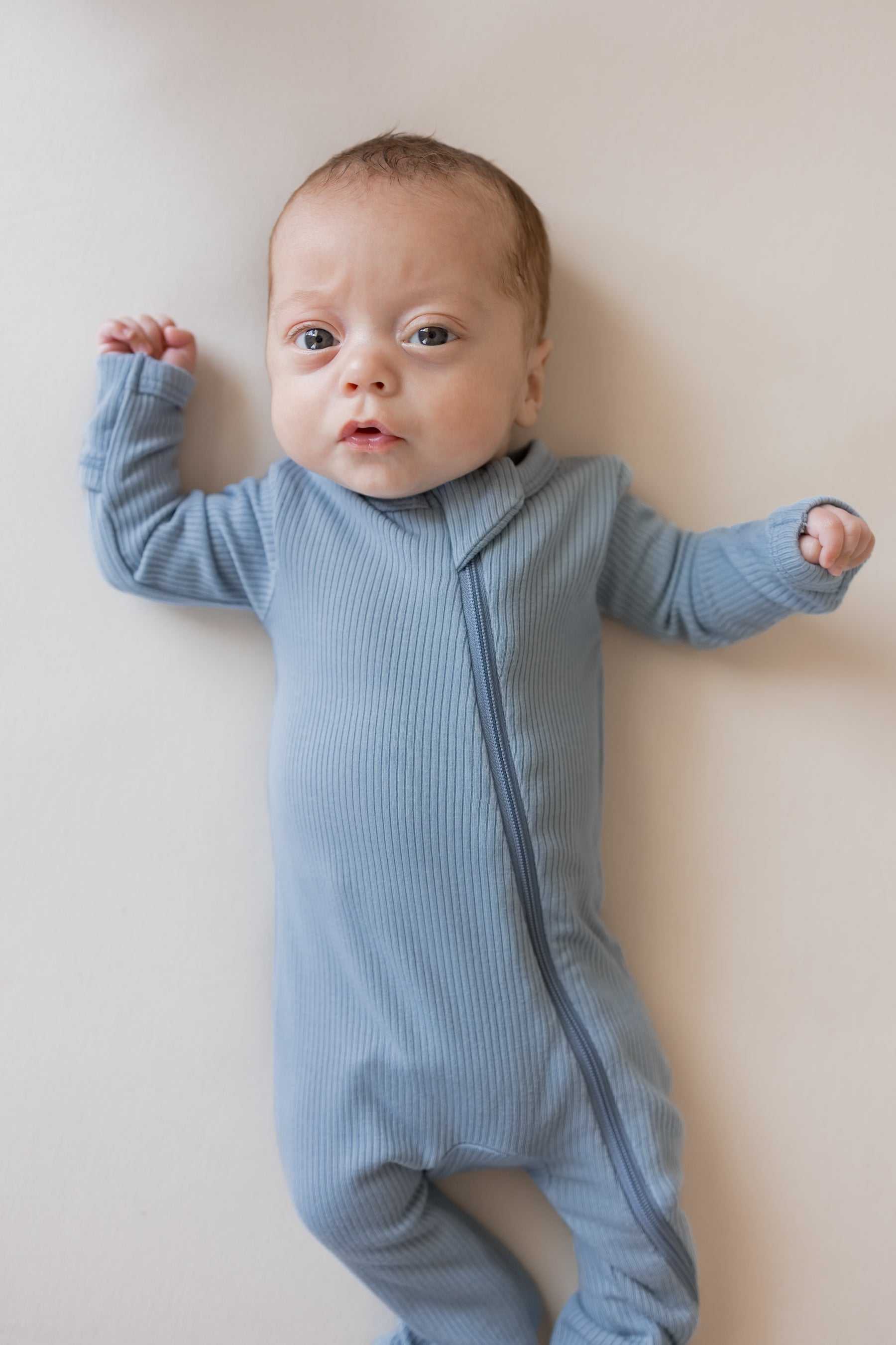 Close up of Baby wearing Ribbed Zippered Romper in Slate color on a beige background