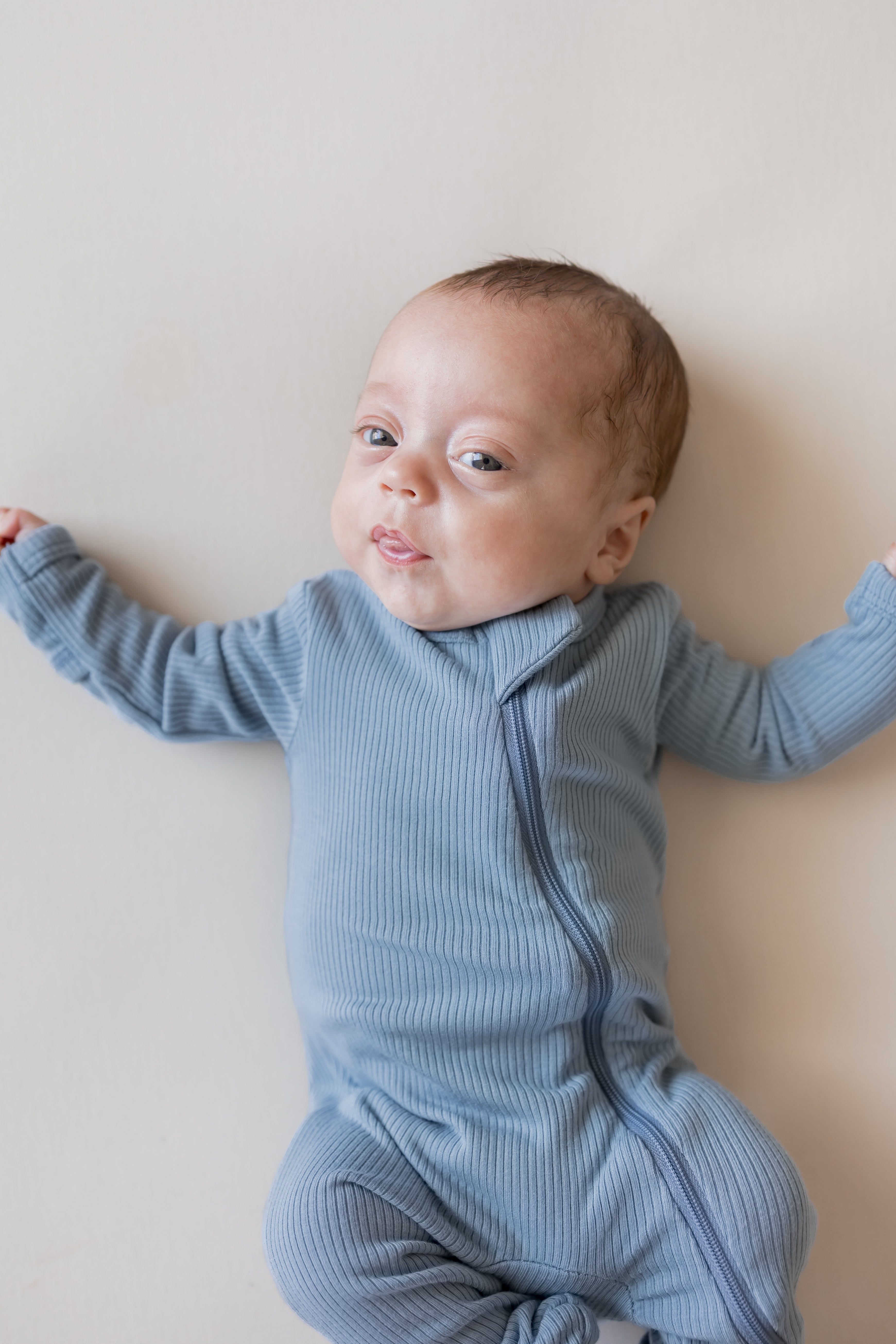 Baby wearing Ribbed Zippered Romper in Slate color lying on a beige background