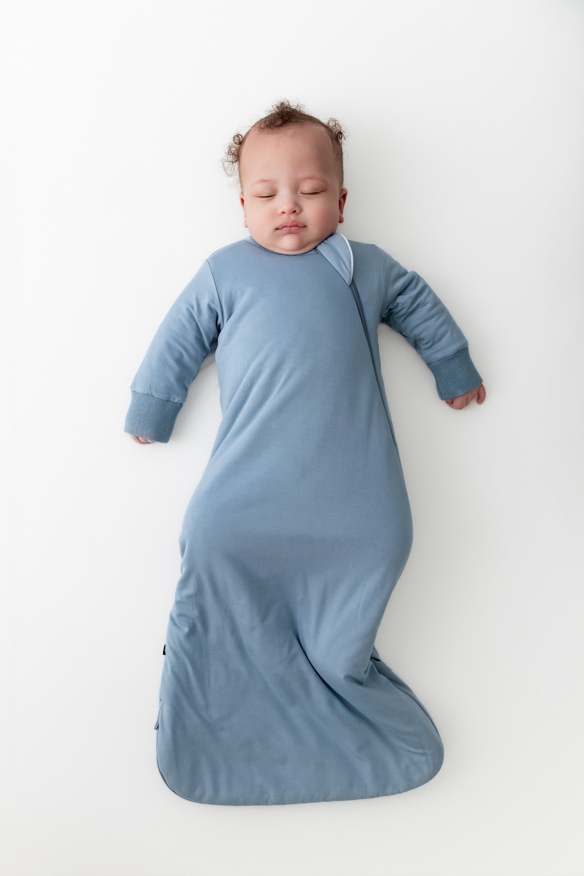 Baby wrapped in a blue slumber bag on a white background