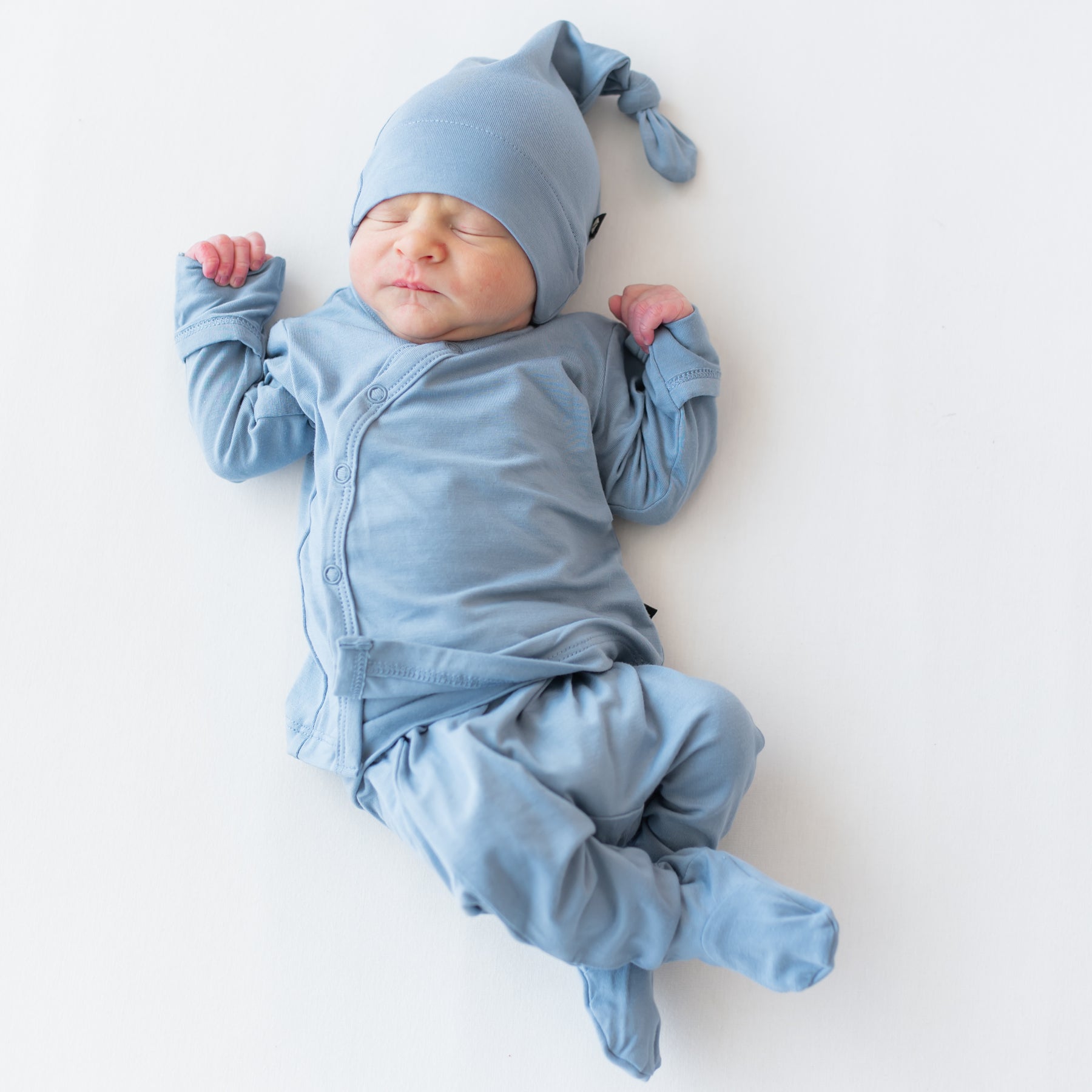 Baby sleeping wearing a take me home set with kimono style top, footie pants and cap in a slate blue