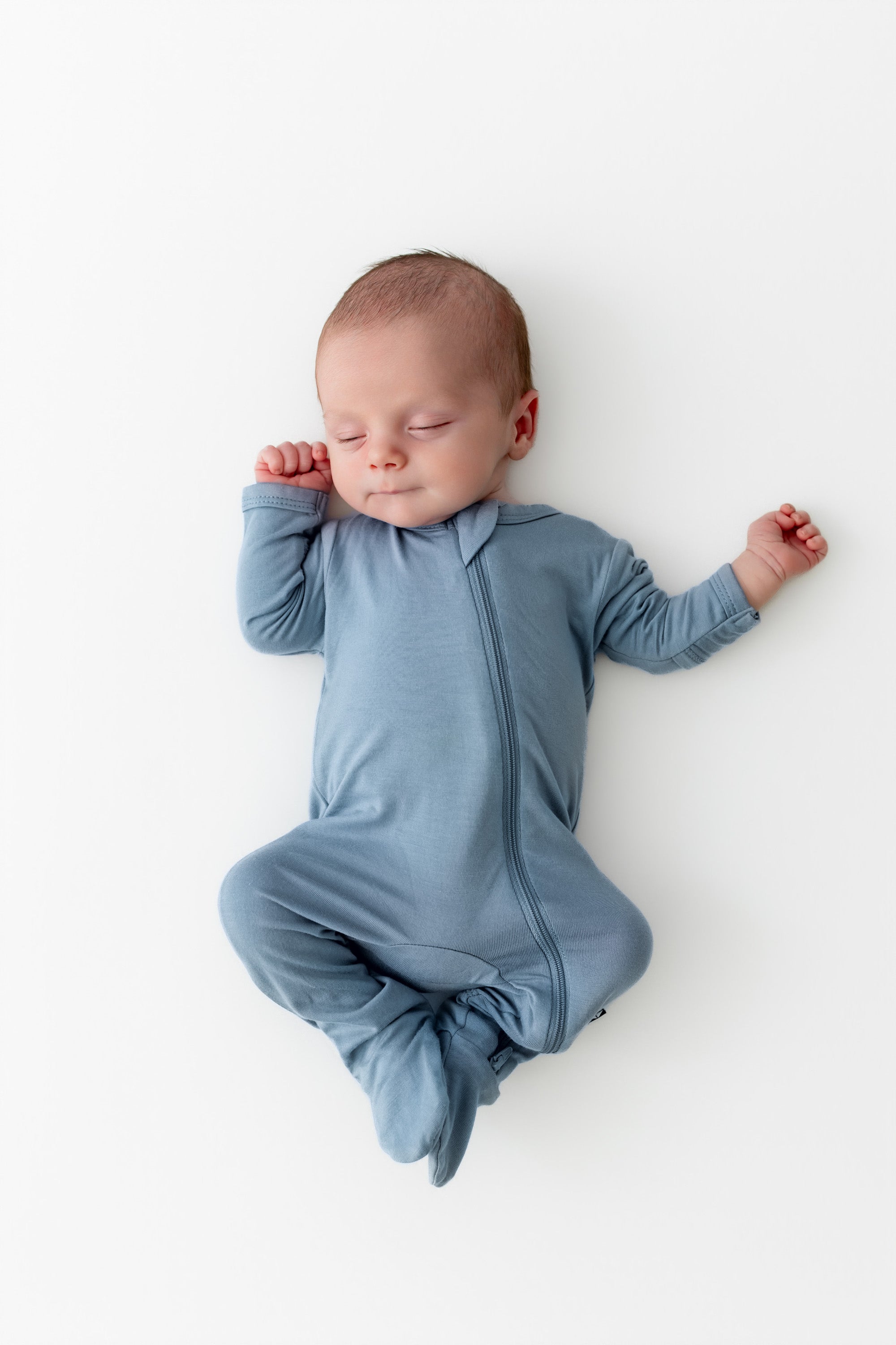 Newborn baby in a blue footie pajama lying on a white background