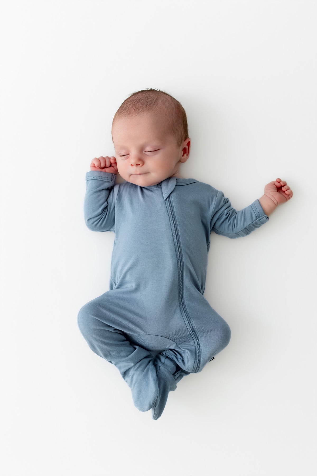 Newborn baby in a blue footie pajama lying on a white background