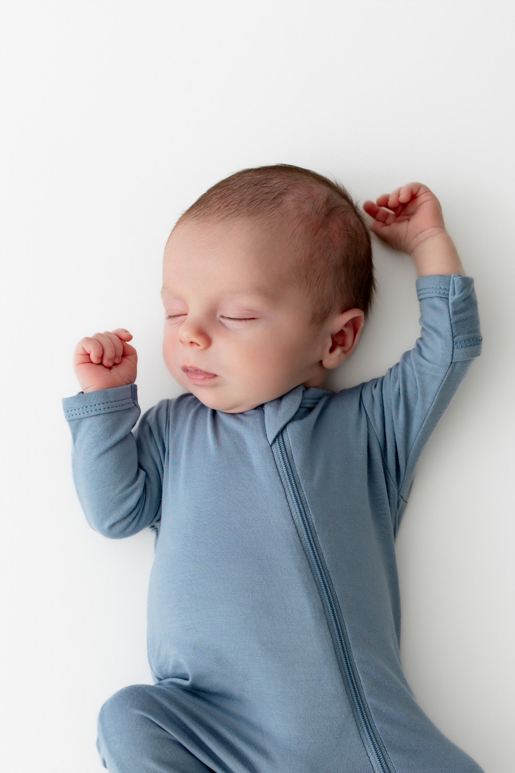 Newborn baby in a blue footie pajama lying on a white surface