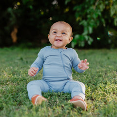 Smiling baby sitting in the grass while wearing a Zippered Romper in Slate
